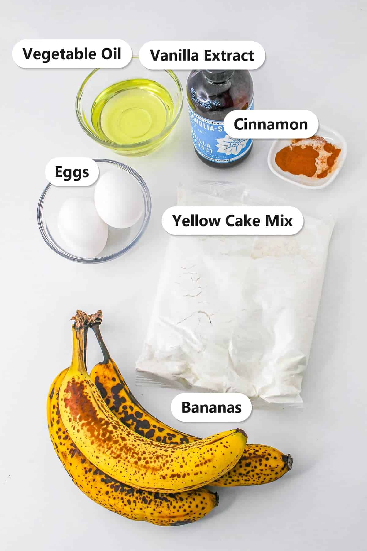Overripe bananas, yellow cake mix, eggs, vegetable oil, vanilla extract, and cinnamon labeled for Banana Cake Mix Muffins.