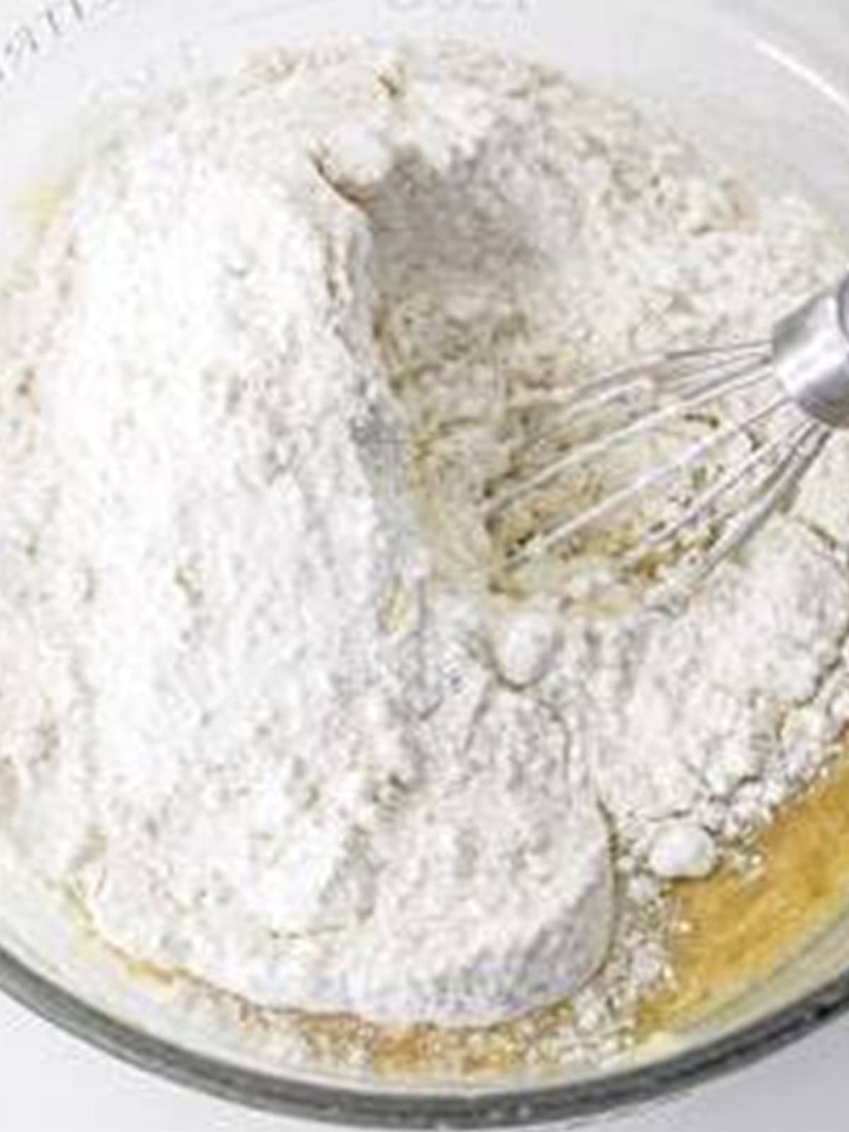 Adding yellow cake mix to the wet banana batter in a bowl.