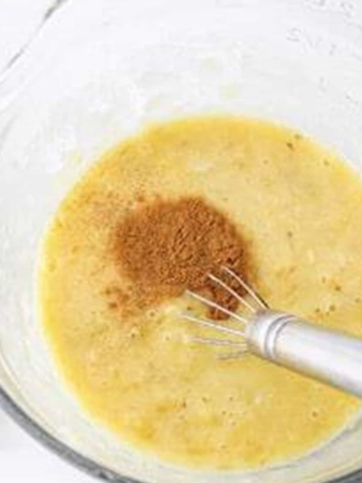 Whisking mashed bananas, eggs, oil, vanilla, and cinnamon in a glass bowl for Banana Cake Mix Muffins.