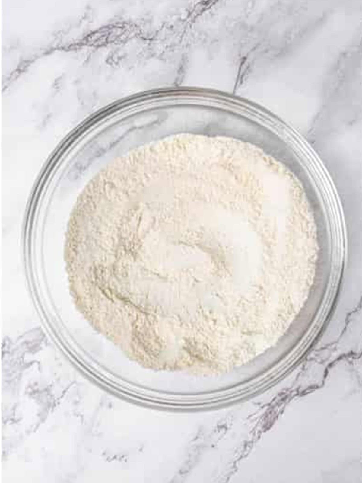 Dry ingredients for banana cake whisked together in a glass bowl.