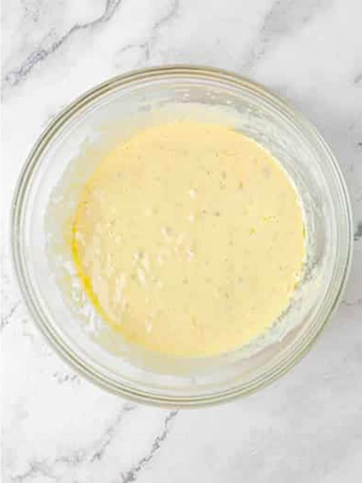 Wet ingredients with mashed banana and vanilla yogurt whisked in a bowl for banana cake.
