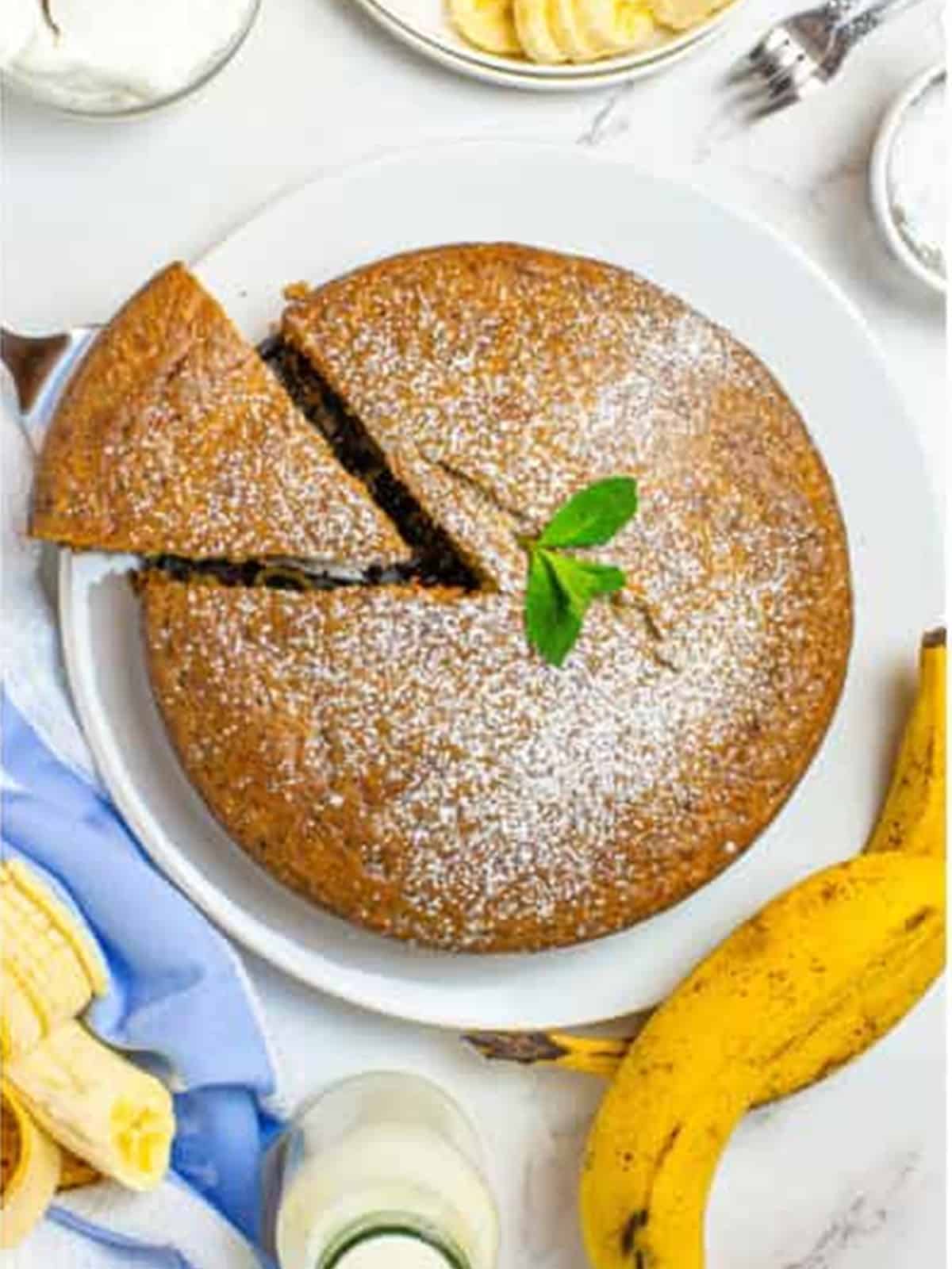 Sliced banana cake on a plate dusted with powdered sugar and fresh banana.