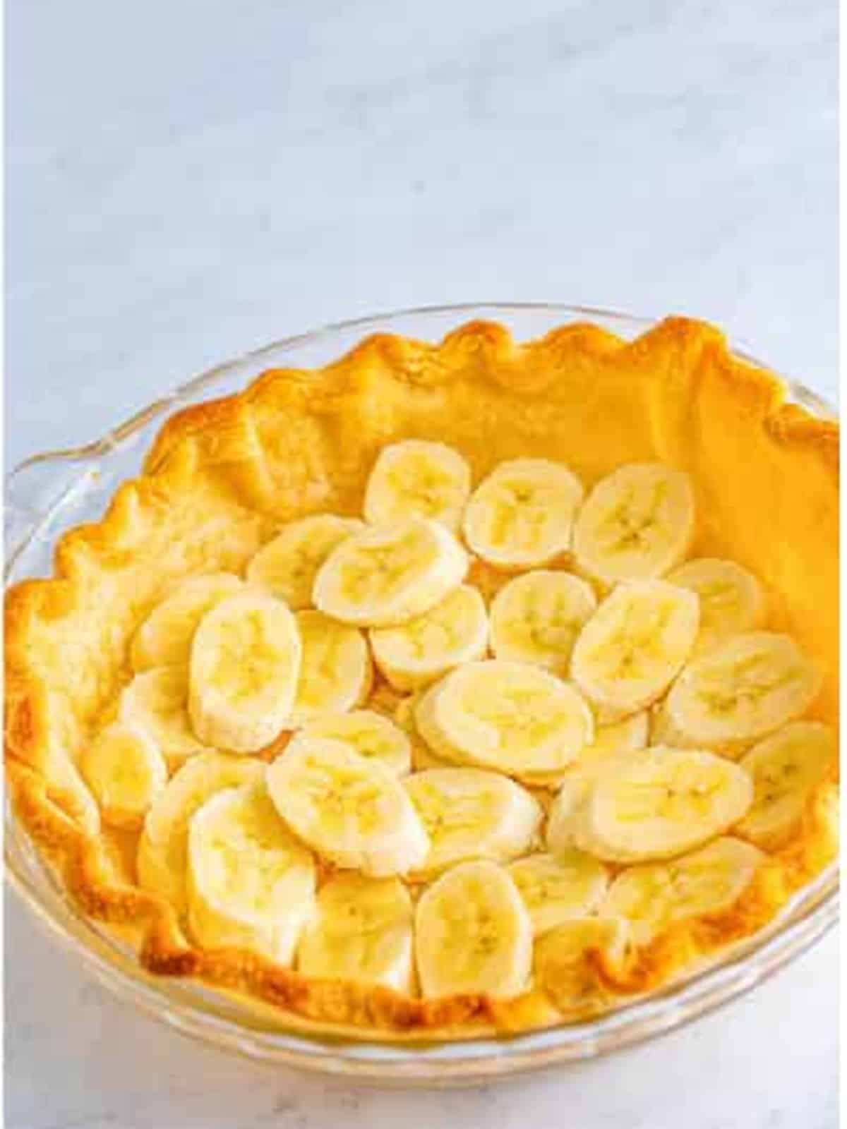 Sliced bananas layered into a baked pie crust for banana cream pie.