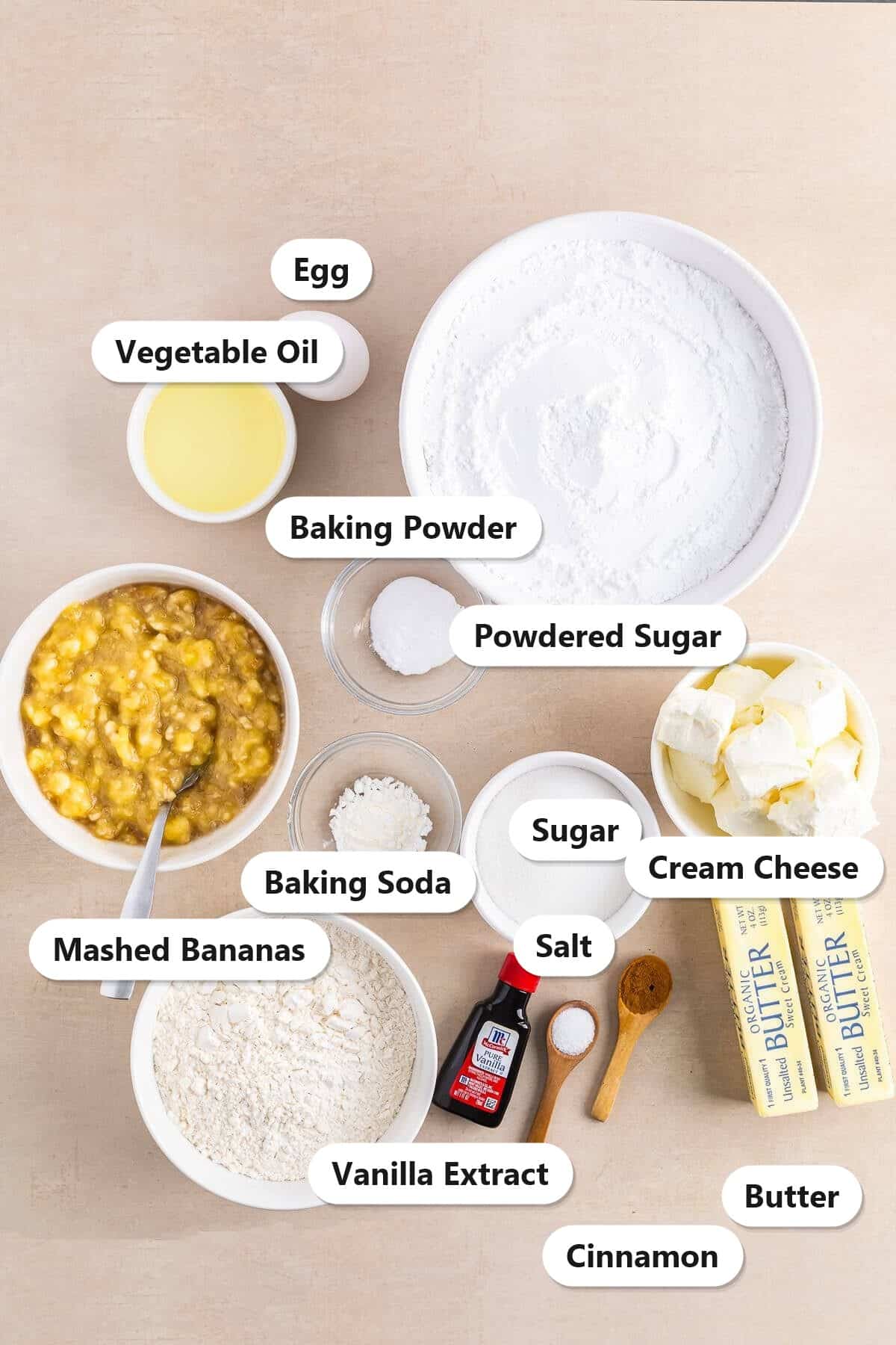 Labeled ingredients for banana cupcakes including mashed bananas, flour, sugar, powdered sugar, cream cheese, butter, egg, vegetable oil, vanilla extract, cinnamon, baking powder, baking soda, and salt.