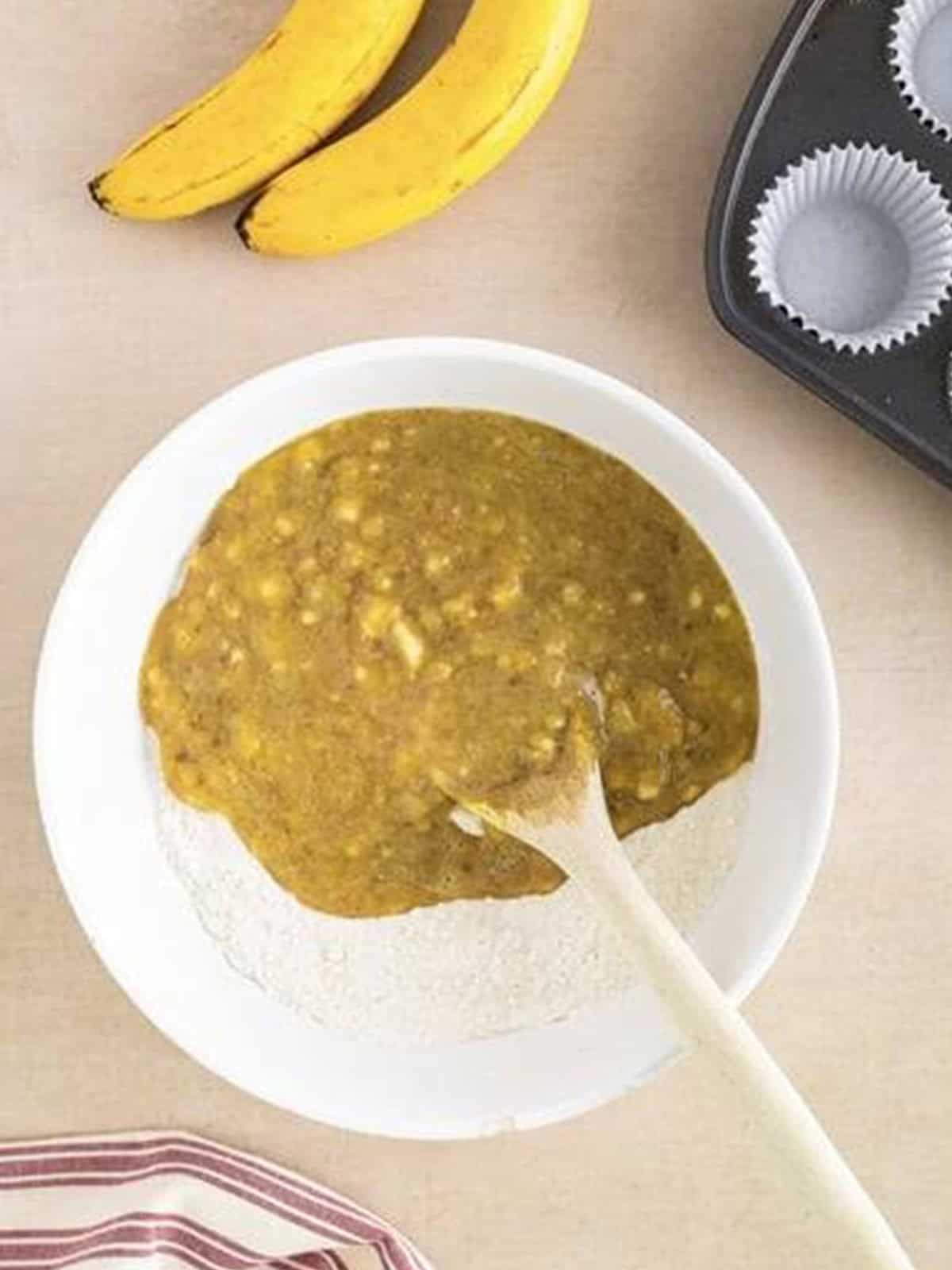 The wet banana mixture poured over the dry ingredients in a mixing bowl.