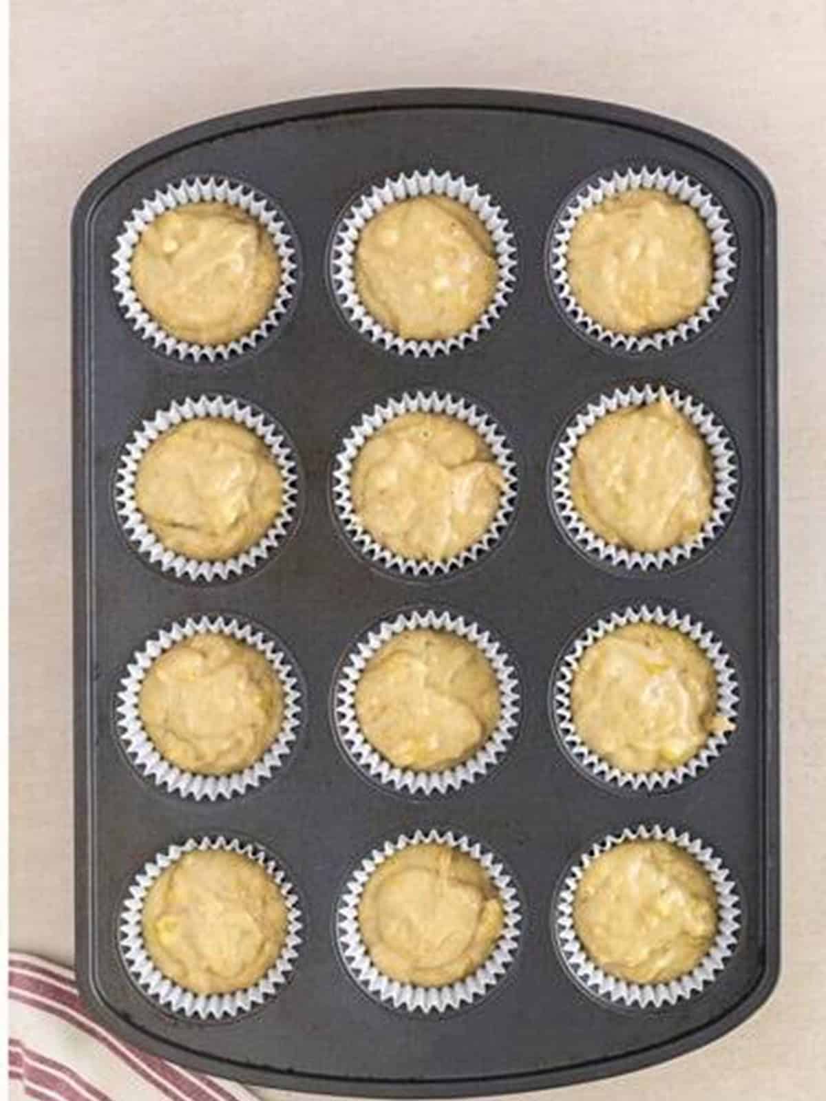 Banana cupcake batter divided evenly between 12 cupcake liners in a muffin tin.