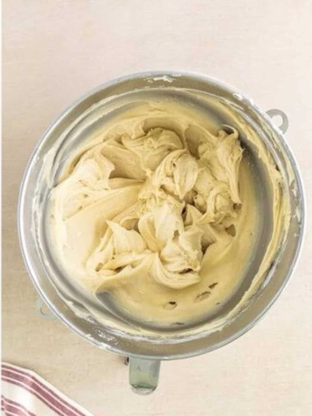 Cream cheese frosting whipped smooth in a stand mixer bowl.