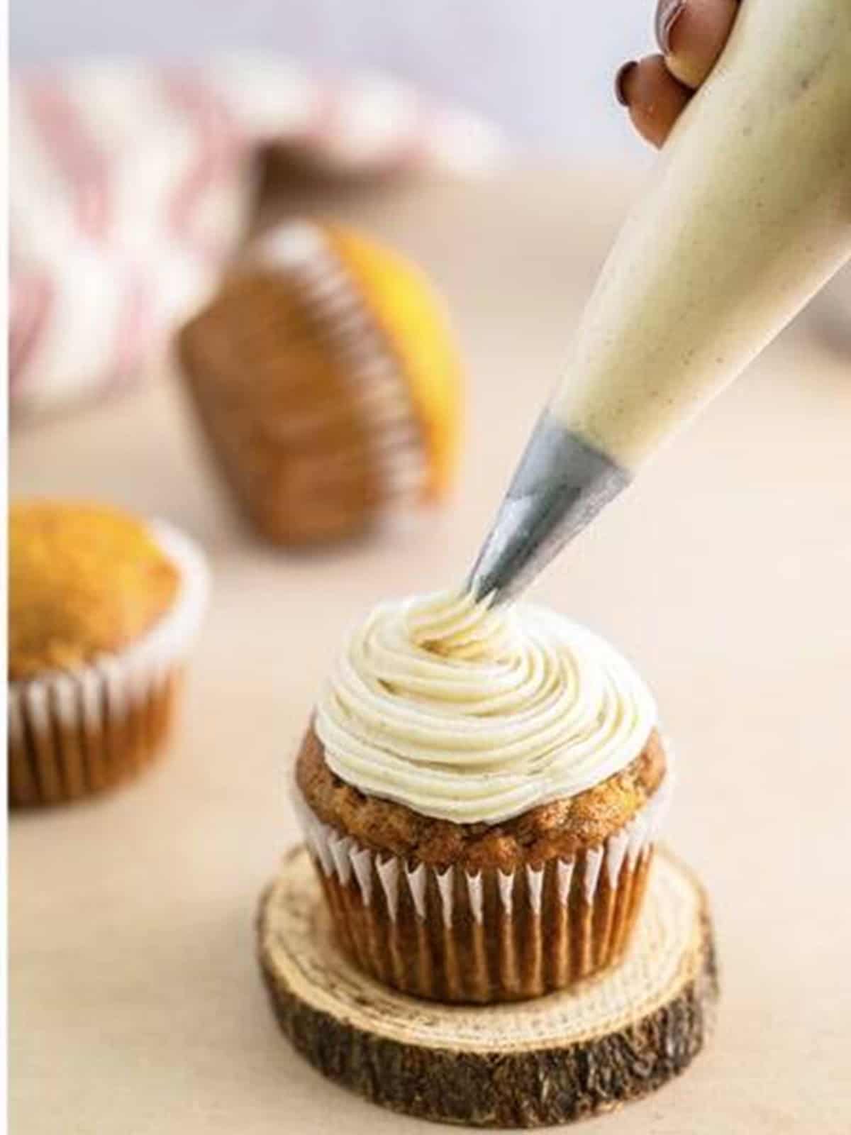 Cream cheese frosting being piped in a swirl onto a banana cupcake.