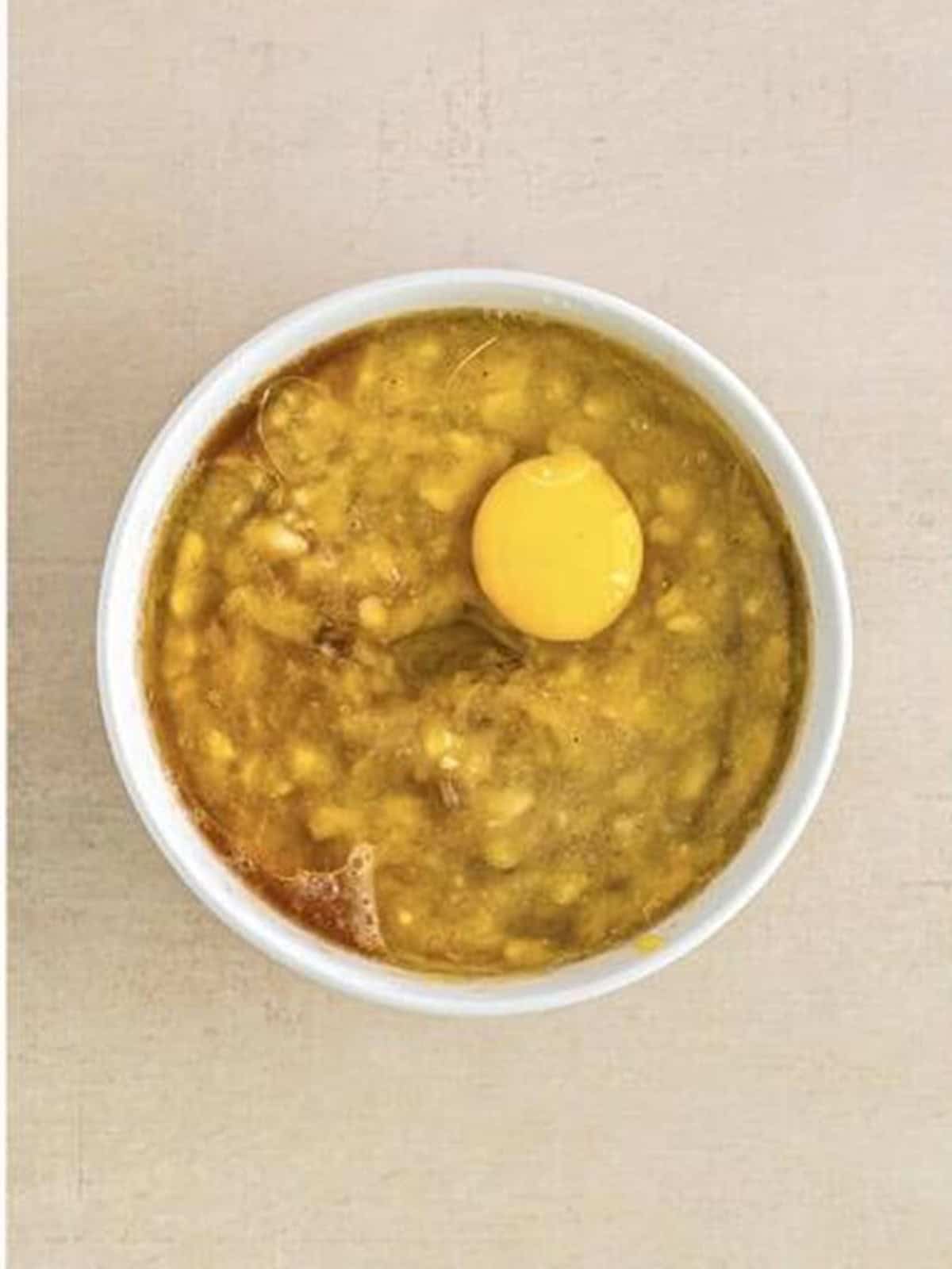 Mashed bananas, oil, vanilla, and an egg in a white bowl ready to whisk.