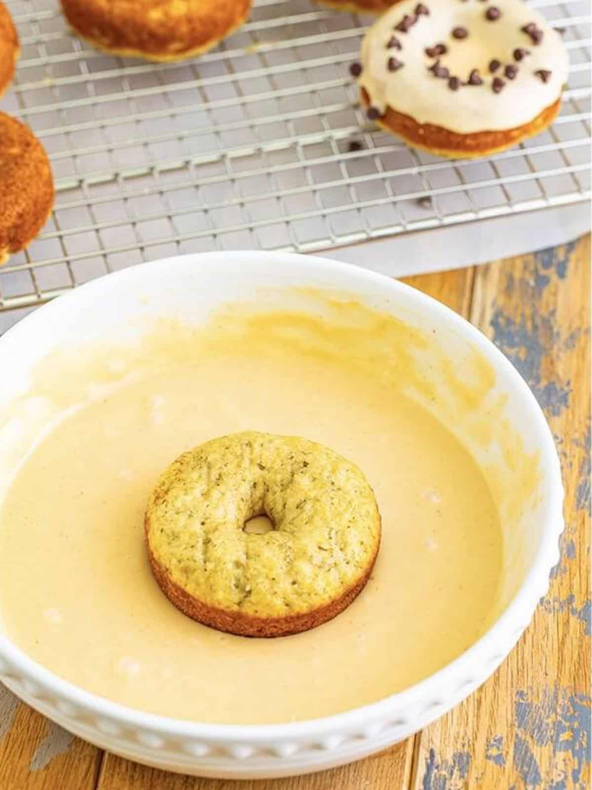 A baked banana donut being dipped into peanut butter glaze.