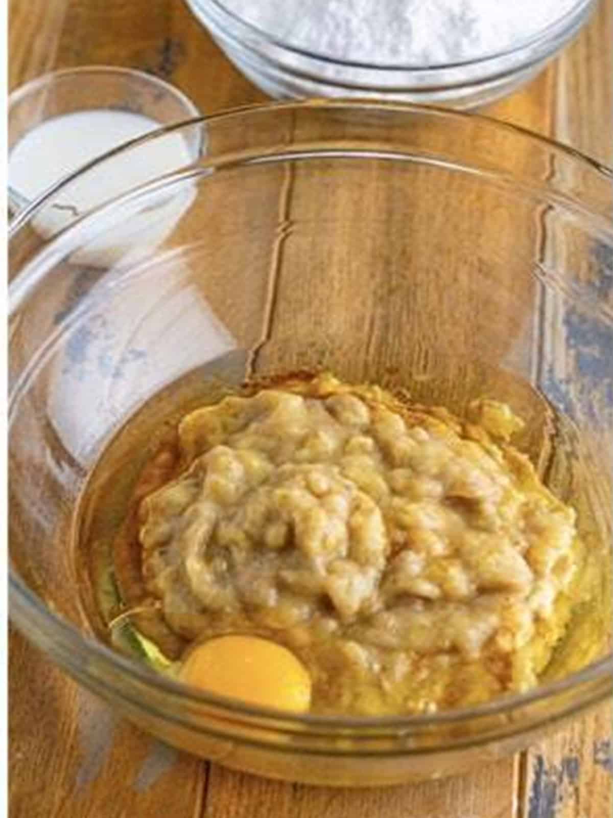 Mashed bananas, egg, and oil mixed in a glass bowl for banana donuts.