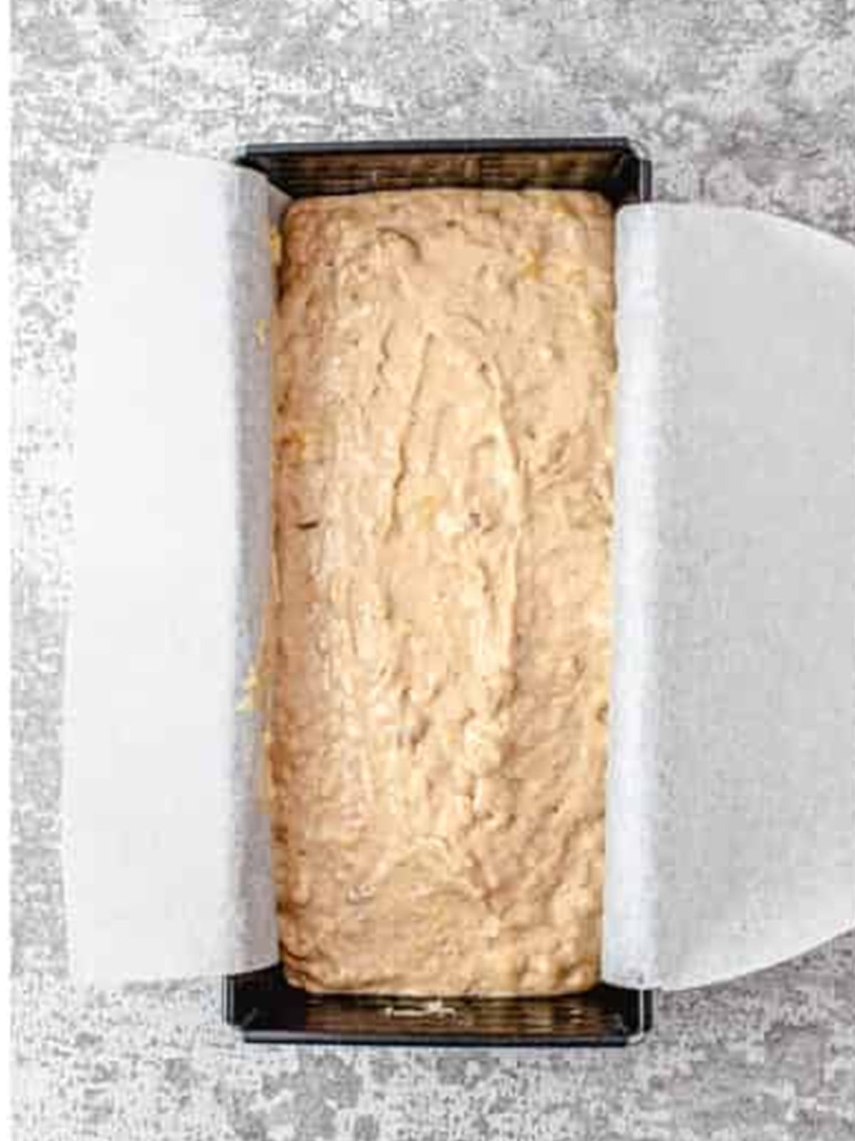 Banana nut bread batter spooned into a parchment-lined loaf pan.