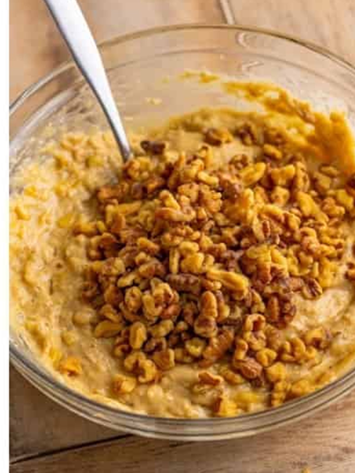 Chopped walnuts being stirred into banana muffin batter.