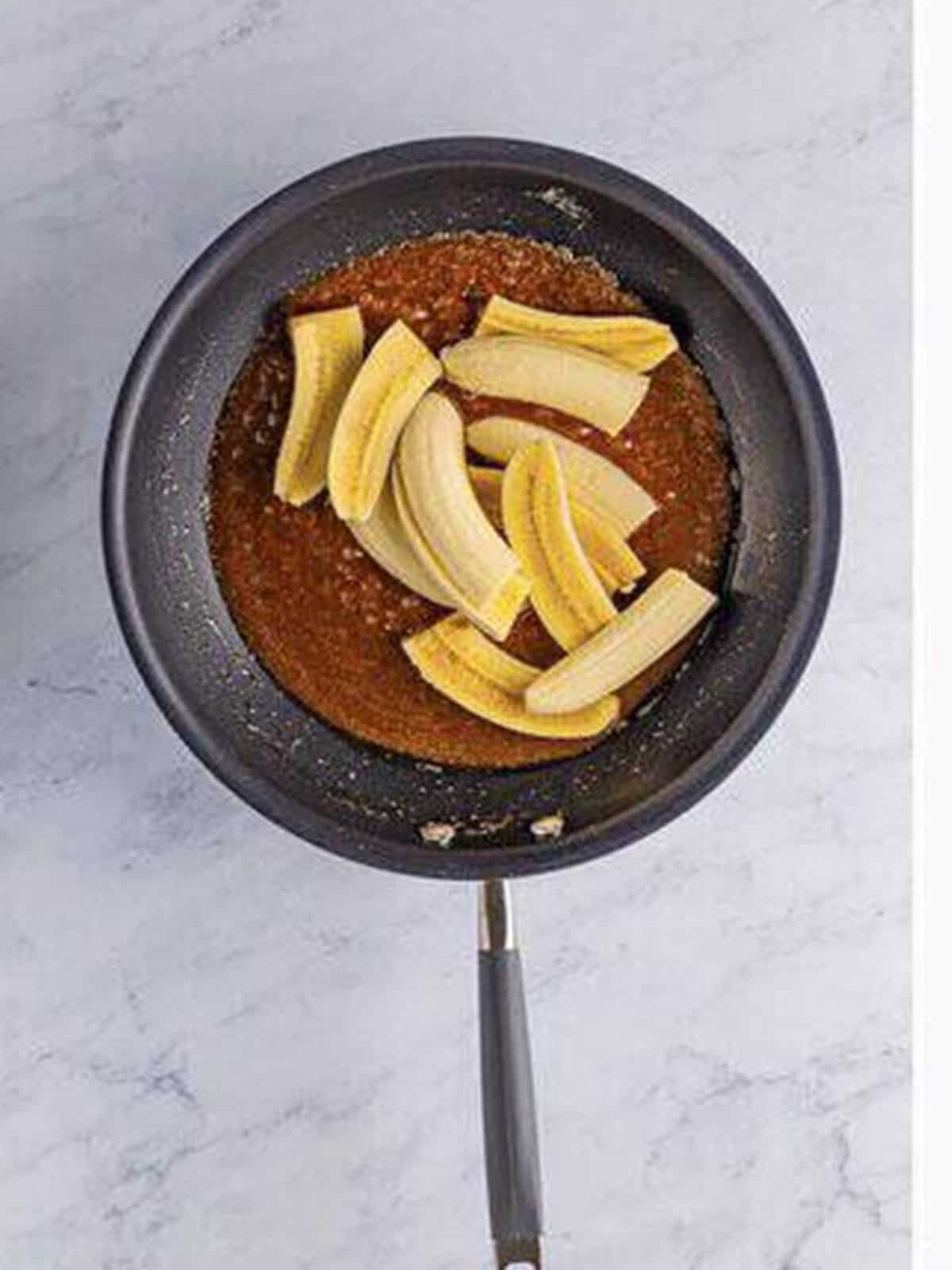 Sliced bananas added to the caramel sauce in a skillet.