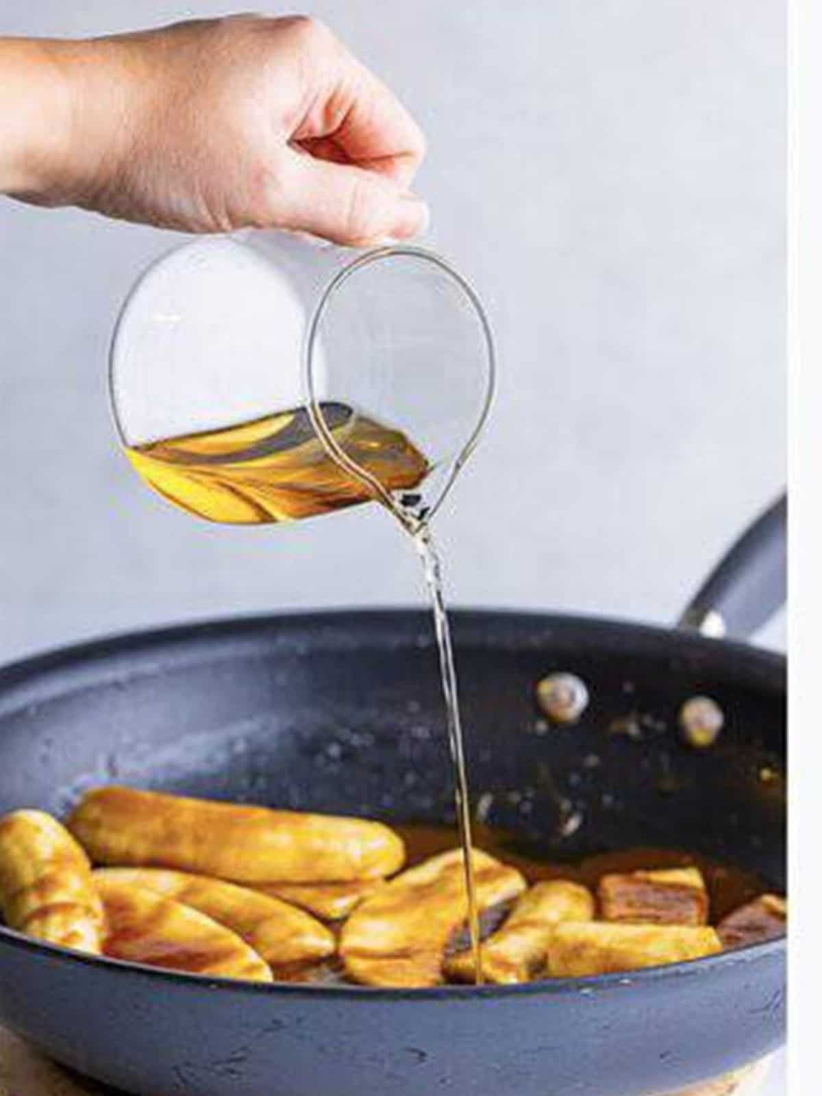 Spiced rum being poured into the skillet of bananas foster.