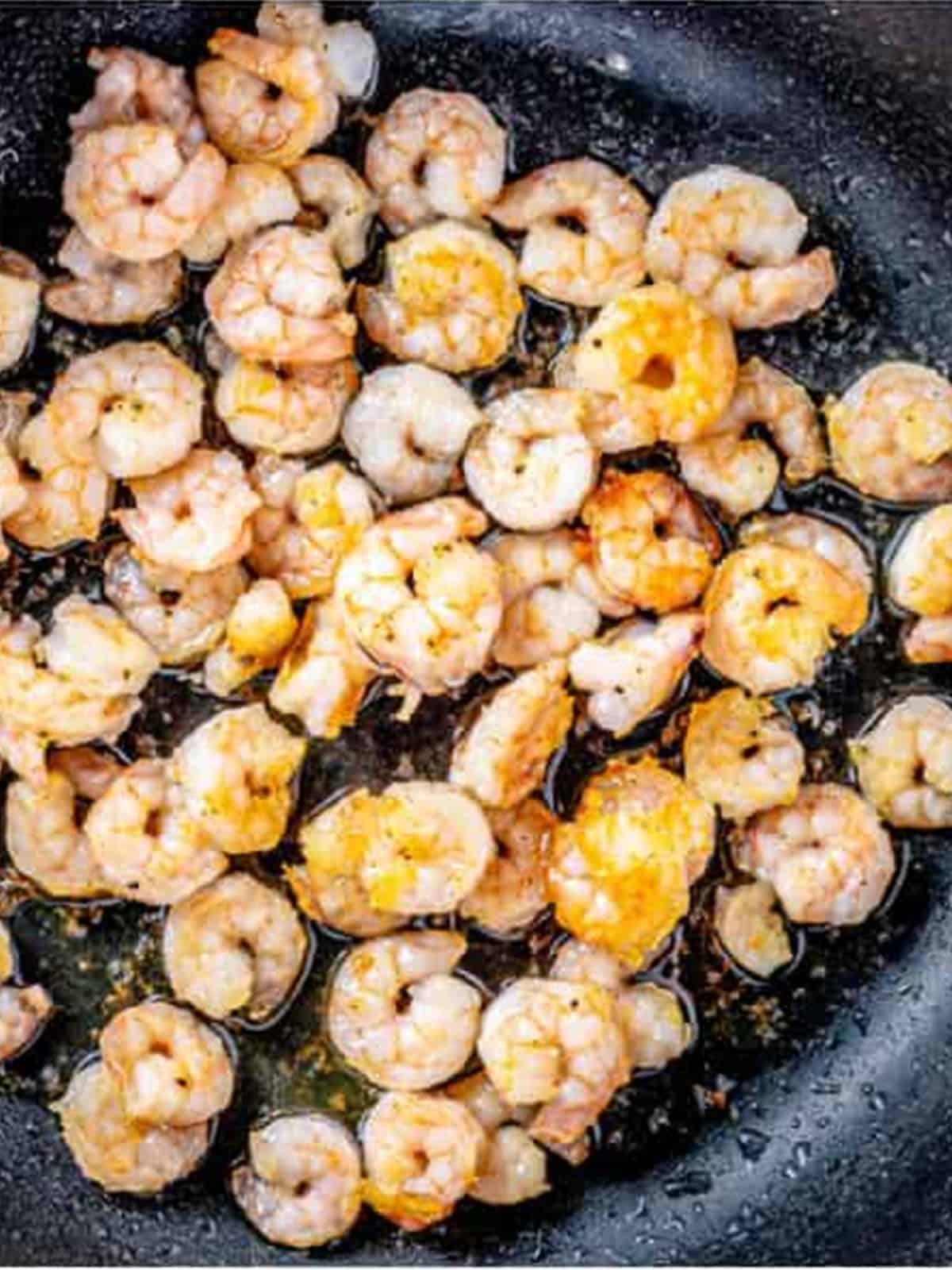 Frying coated shrimp in a skillet until crispy and golden.
