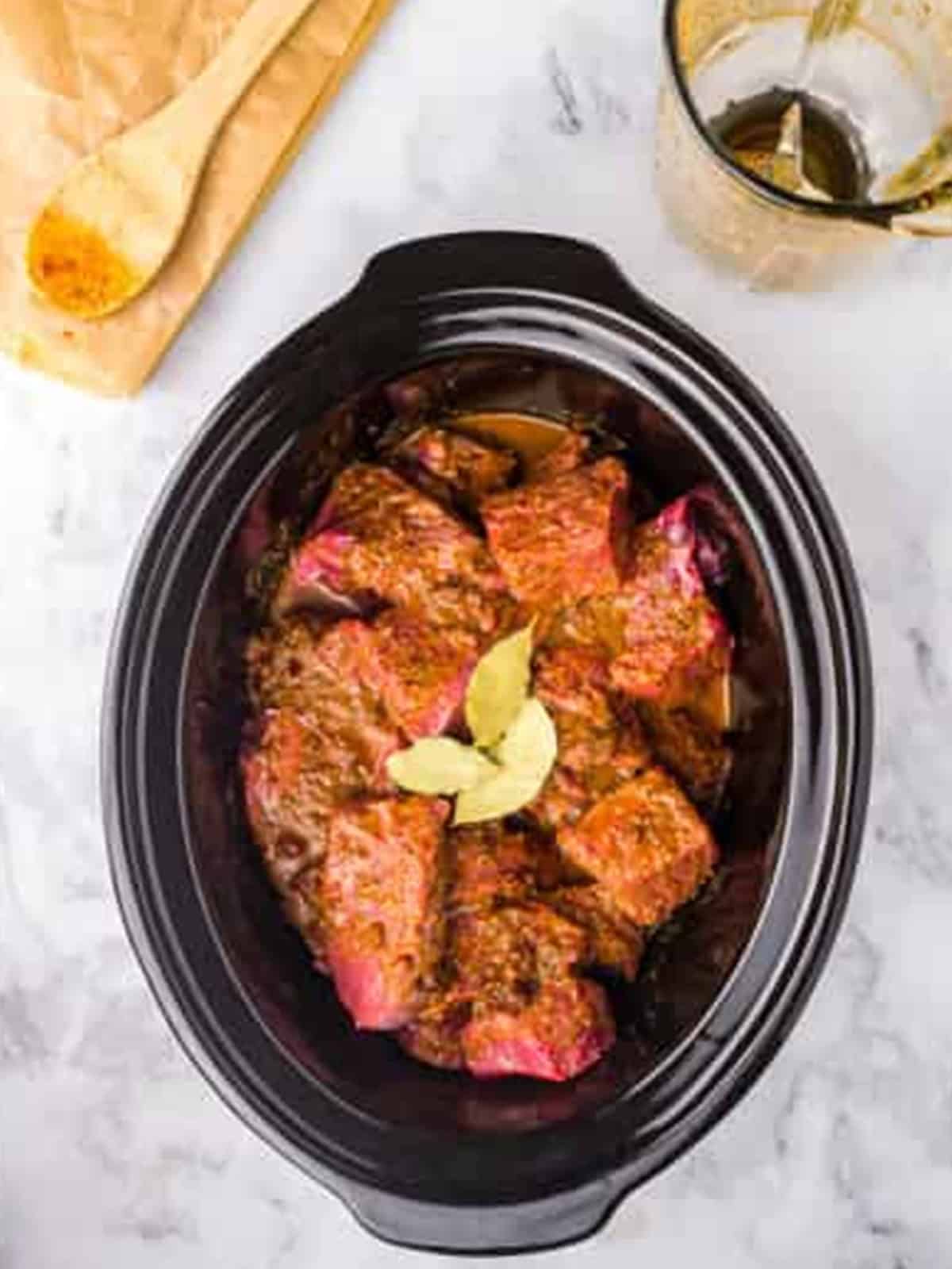 Seasoned barbacoa beef with bay leaves in the slow cooker before cooking.