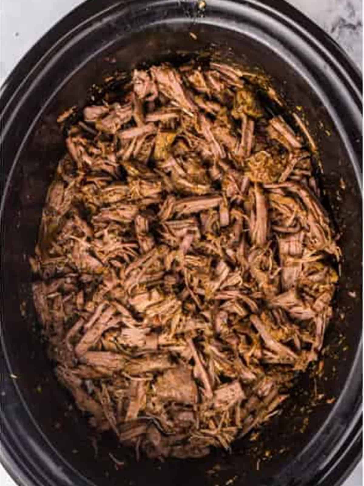 Finished shredded barbacoa in the slow cooker ready to serve in tacos.