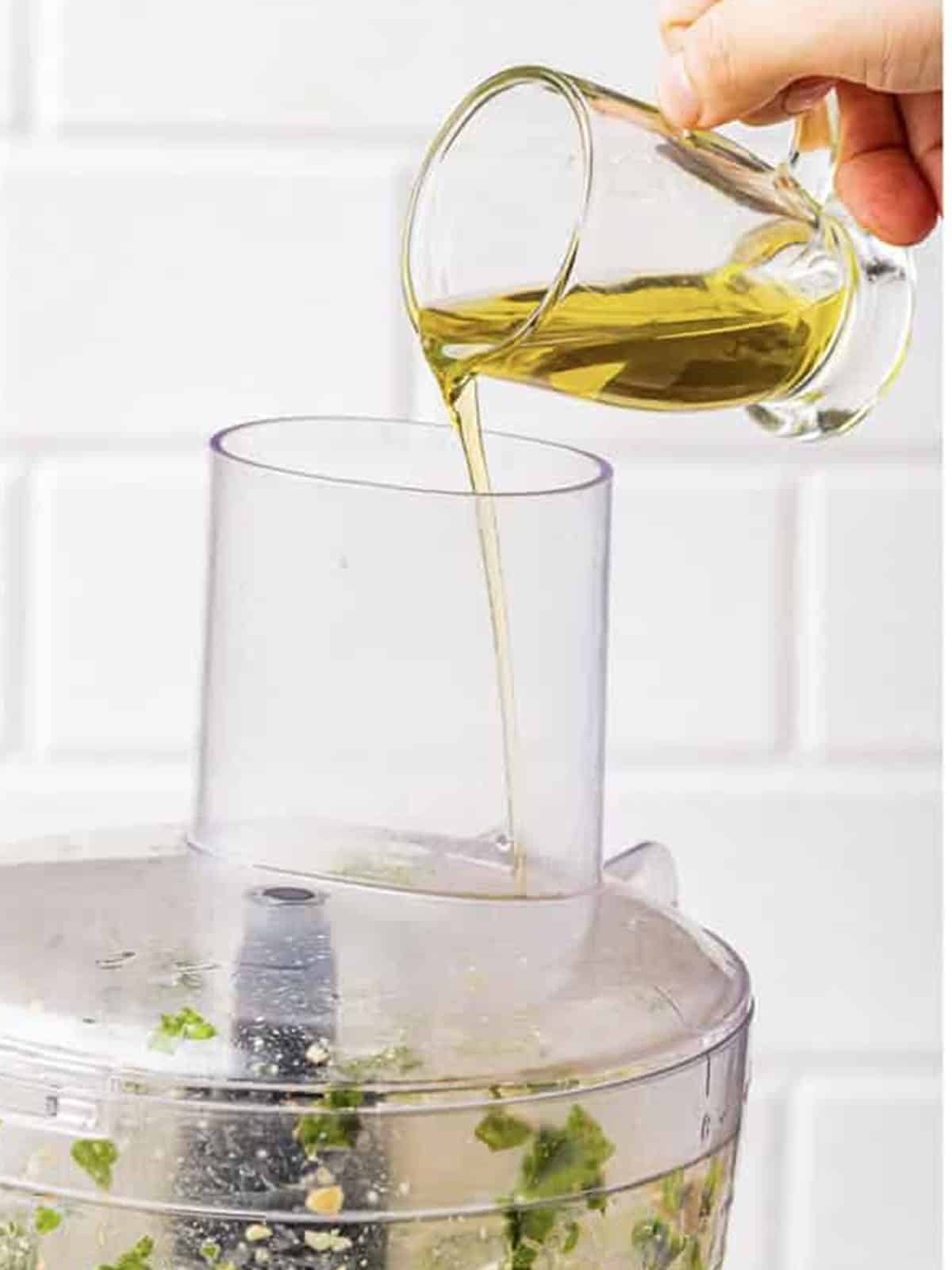 Olive oil being streamed into a food processor while making pesto sauce.