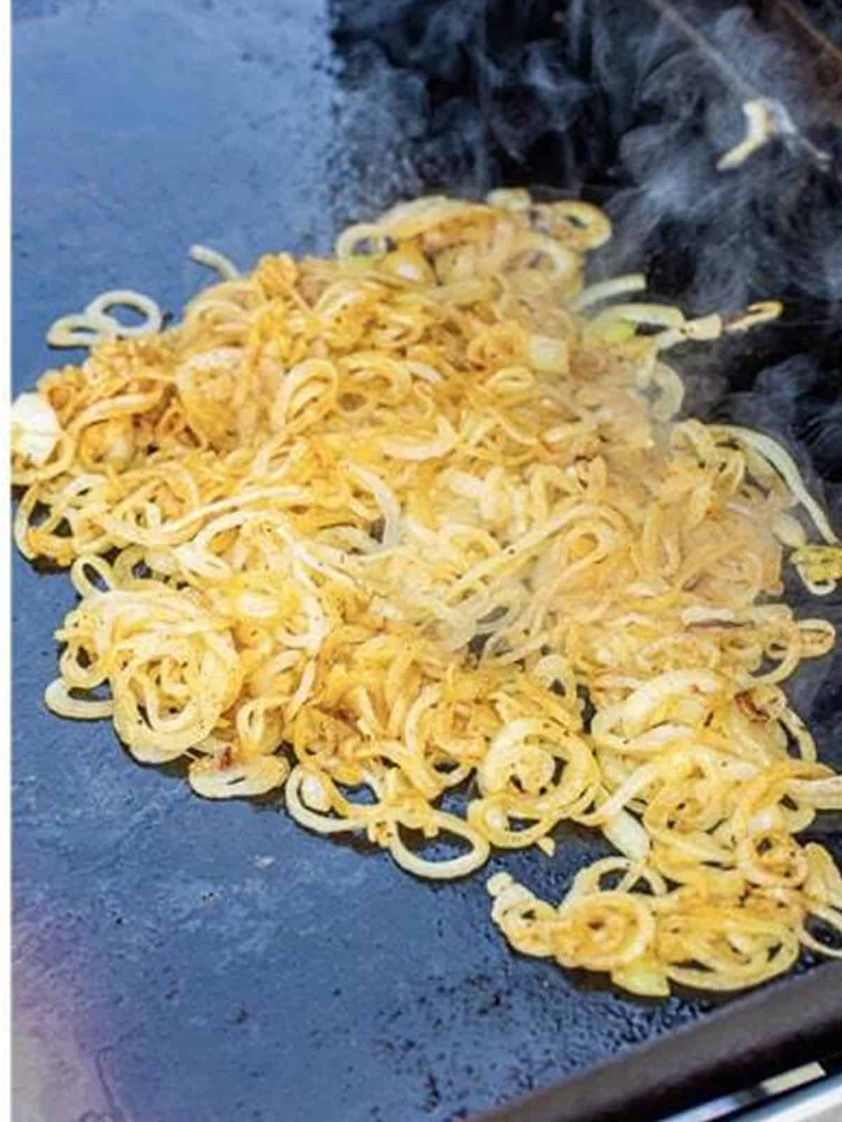 Sliced onions caramelizing in butter on the griddle.