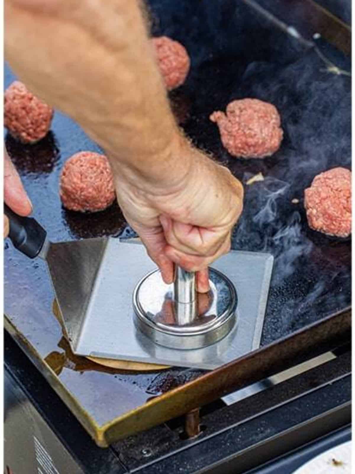 A beef ball being smashed thin on the griddle with a weight.
