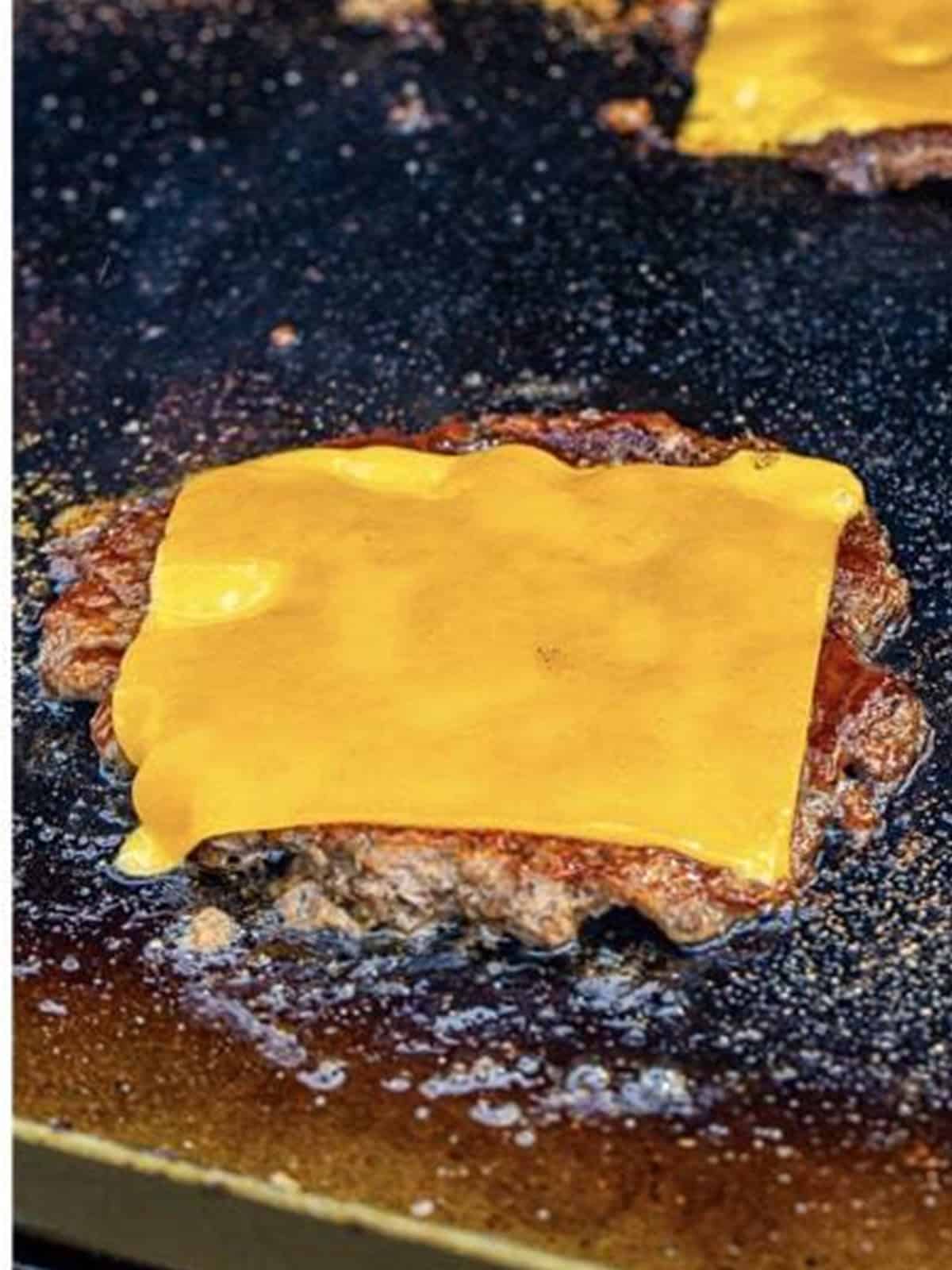 A slice of cheddar cheese melting over a smash burger patty.