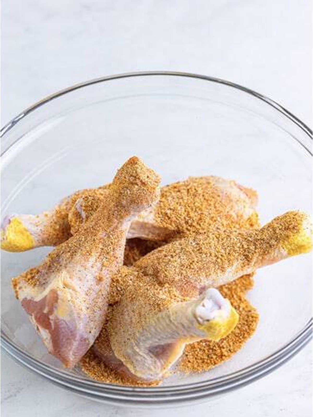 Raw chicken legs tossed with the spice rub in a bowl.