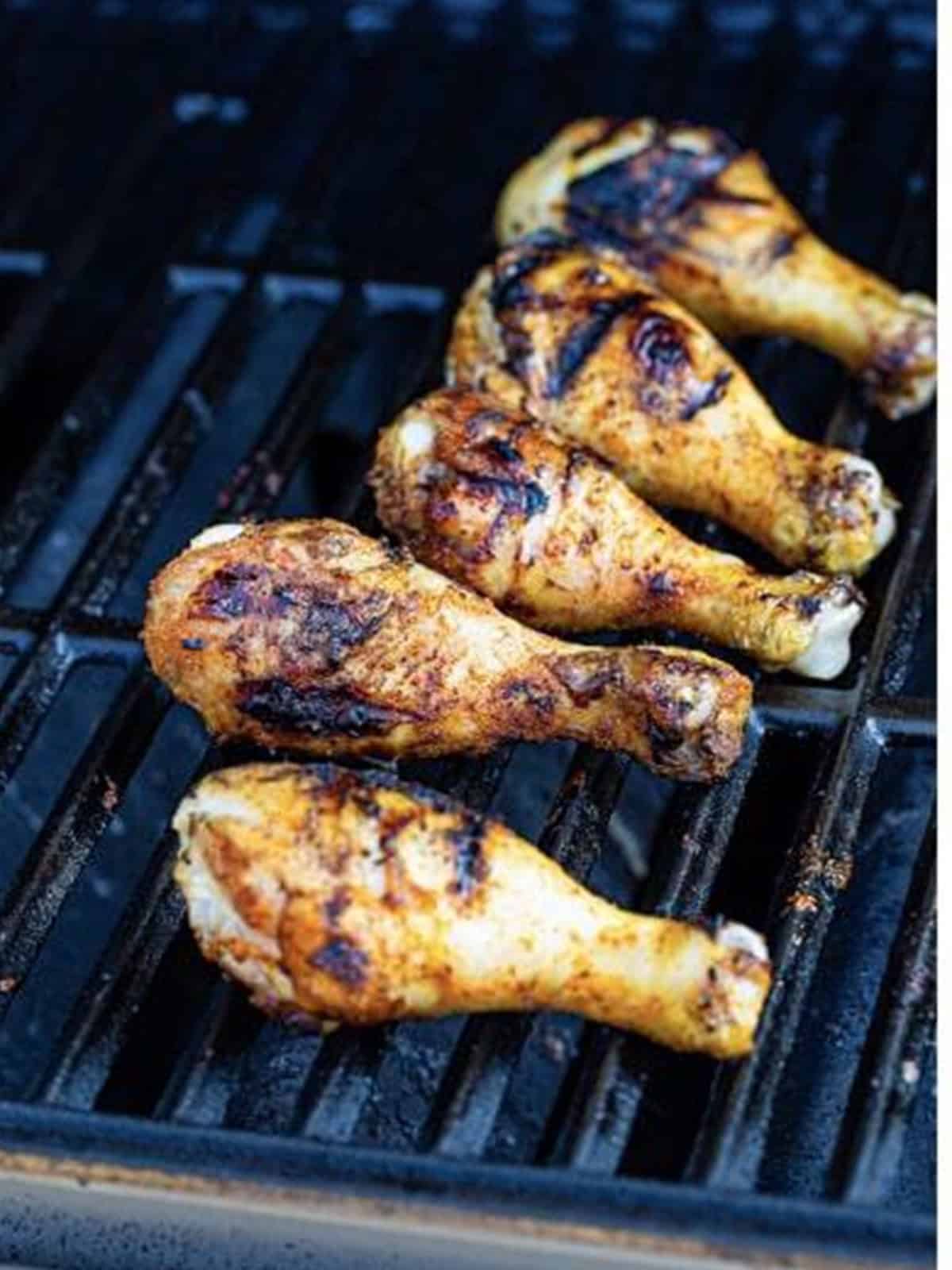 Seasoned chicken legs cooking on a grill.