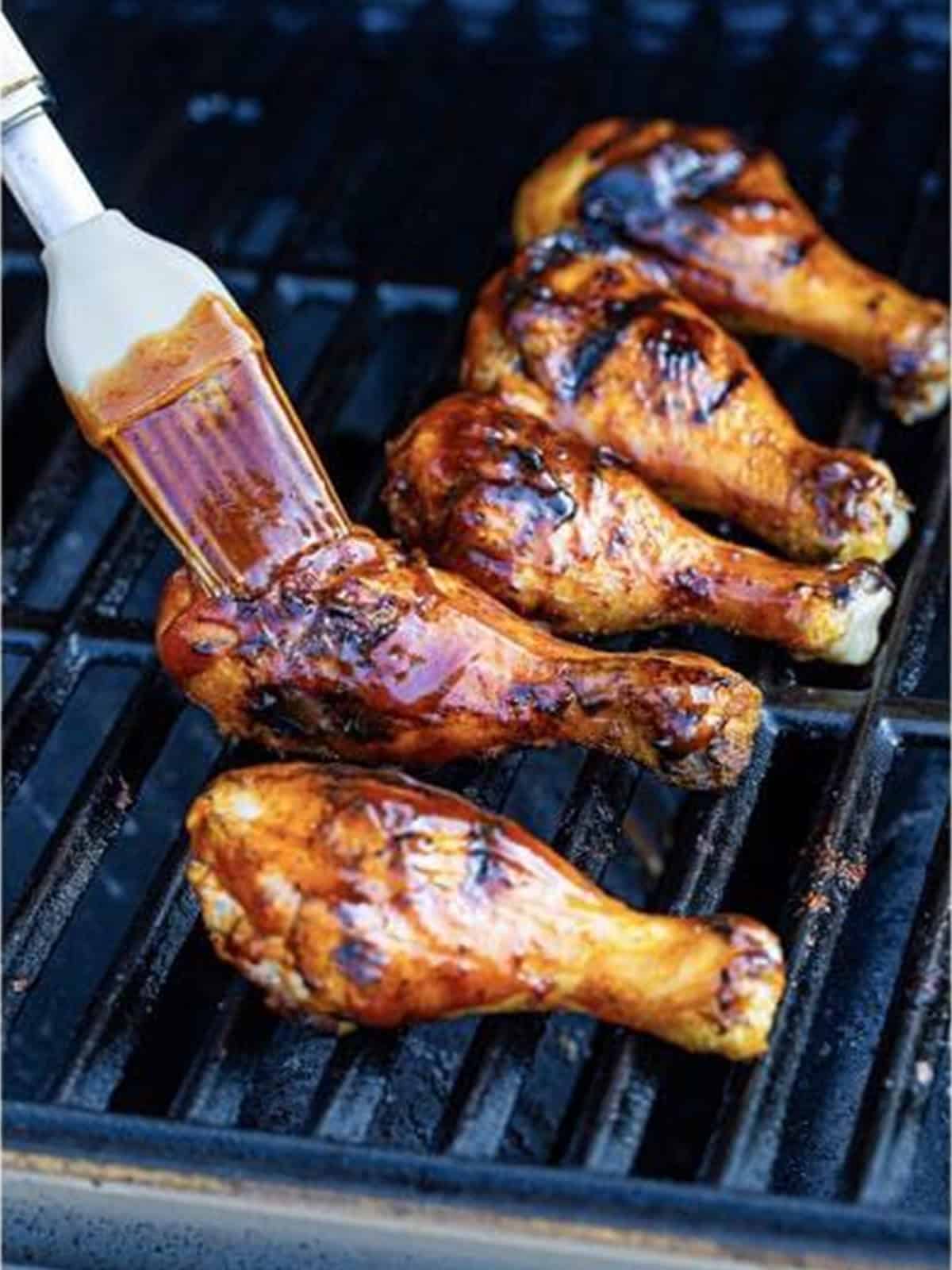 Chicken legs being basted with BBQ sauce on the grill.