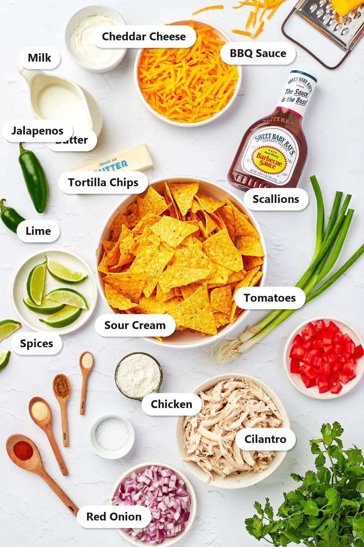 Labeled ingredients for BBQ chicken nachos including tortilla chips, shredded chicken, cheddar cheese, BBQ sauce, milk, butter, and fresh toppings.