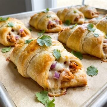 Golden baked BBQ chicken pizza crescent rolls on a baking sheet garnished with cilantro.