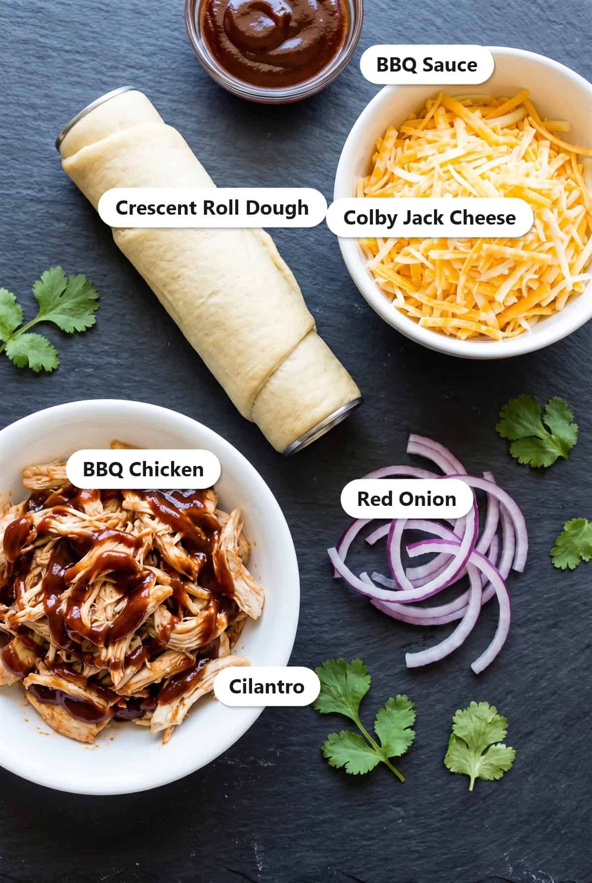 Labeled ingredients for BBQ chicken pizza crescent rolls including crescent dough, BBQ sauce, colby jack cheese, shredded BBQ chicken, red onion, and cilantro.
