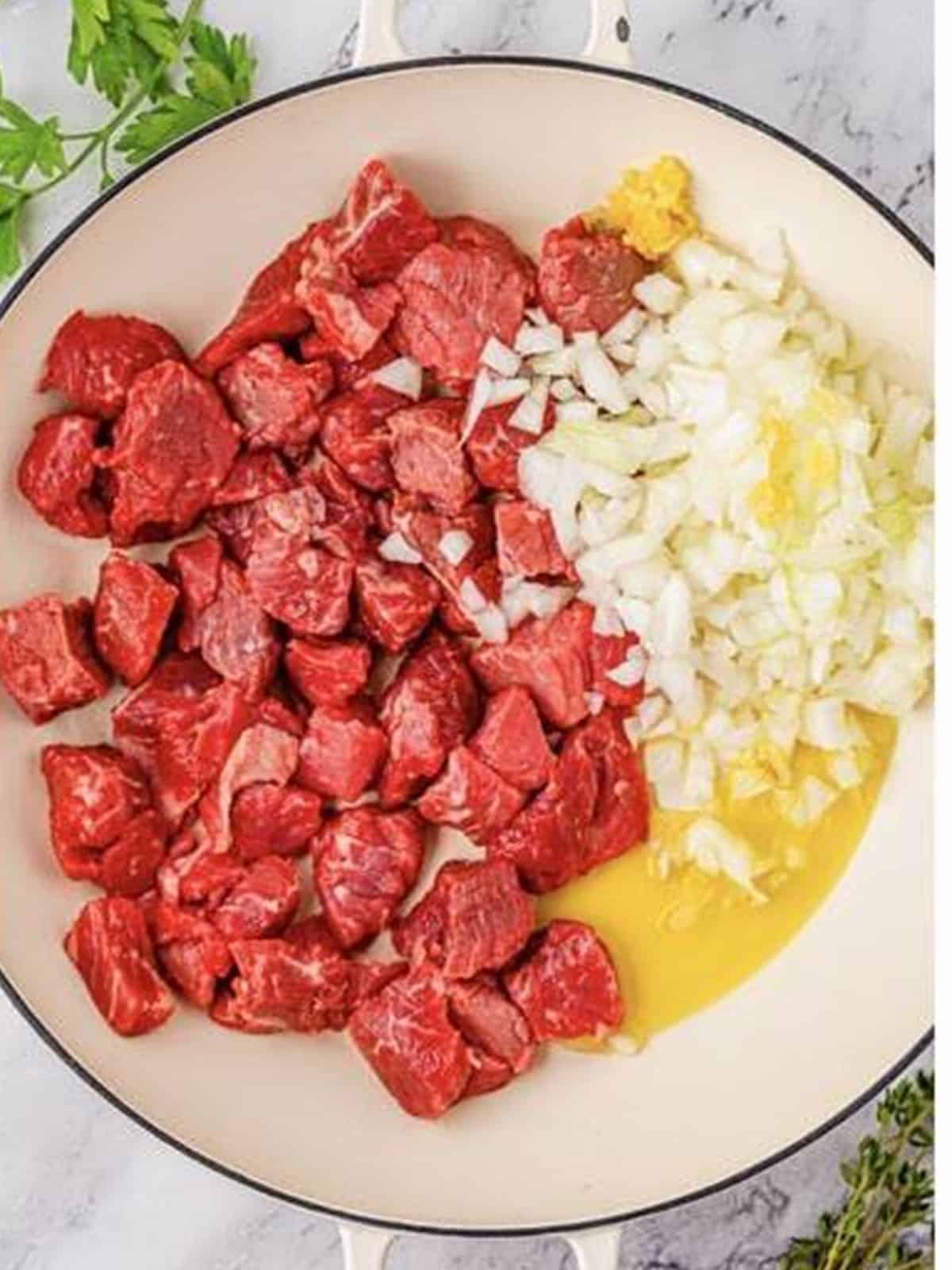 Beef stew meat, diced onion, and olive oil added to a skillet for beef barley soup.
