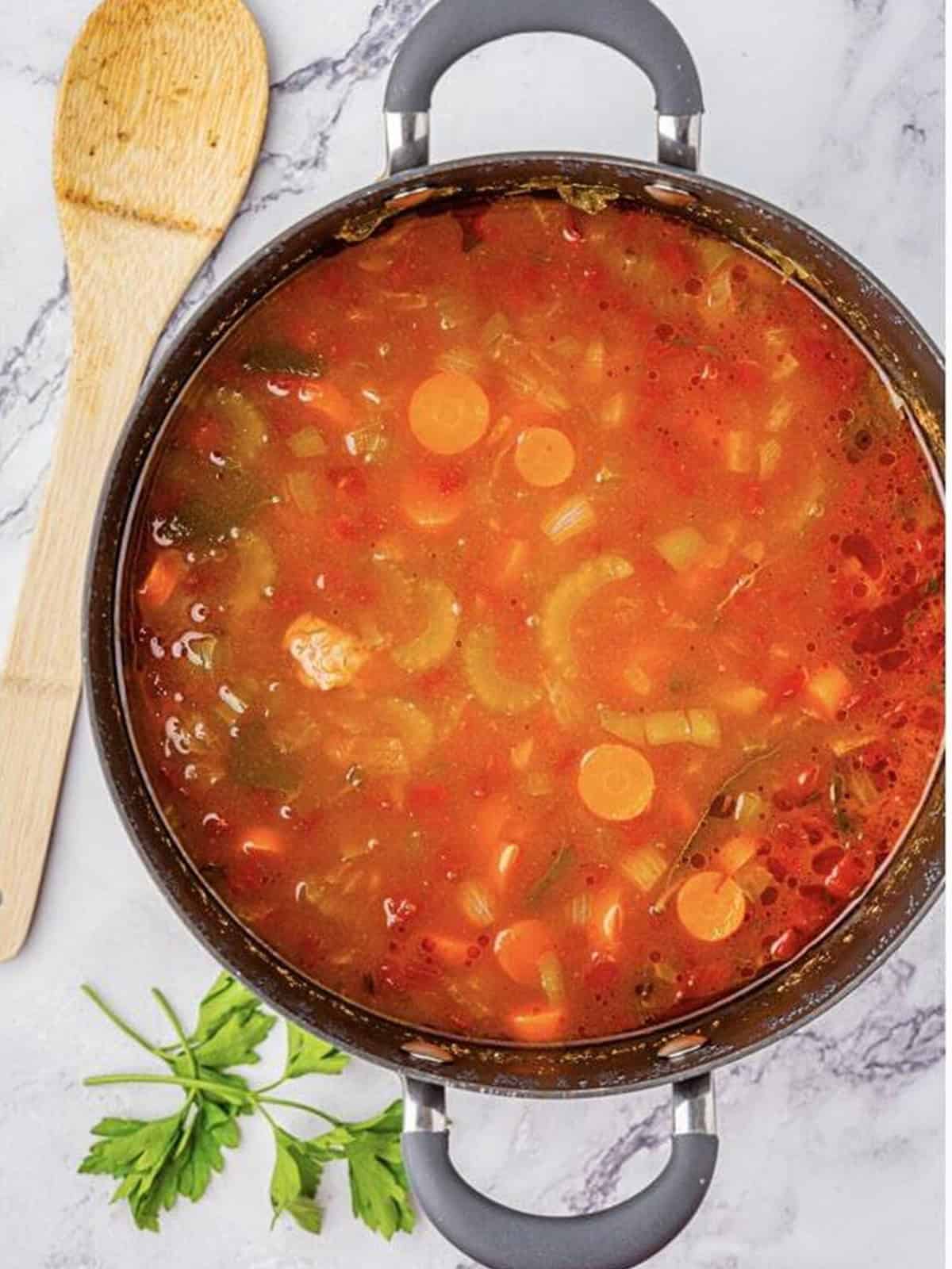 Beef barley soup simmering with tomatoes and vegetables in a large pot.