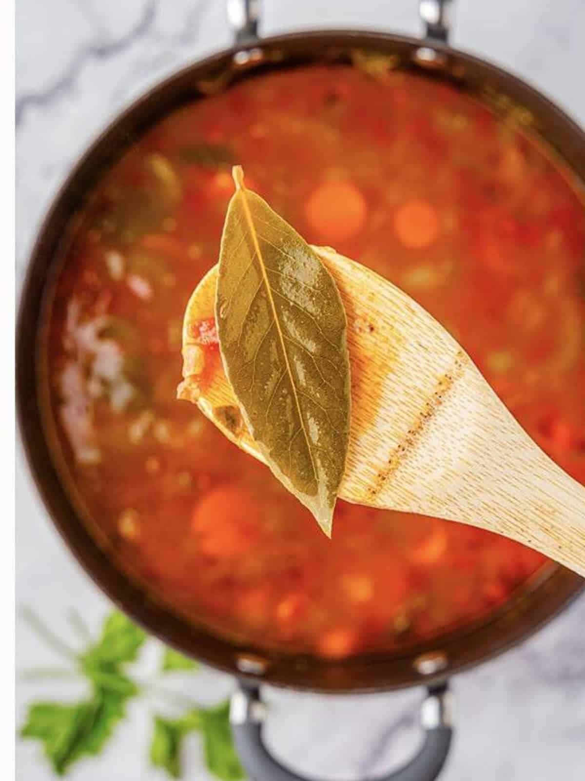 Finished beef barley soup with a bay leaf lifted on a wooden spoon.