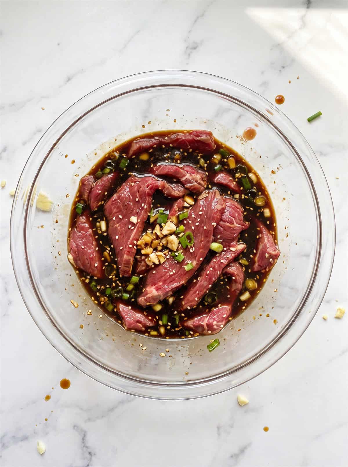 Thin slices of flank steak marinating in a dark Asian soy hoisin marinade in a glass bowl.