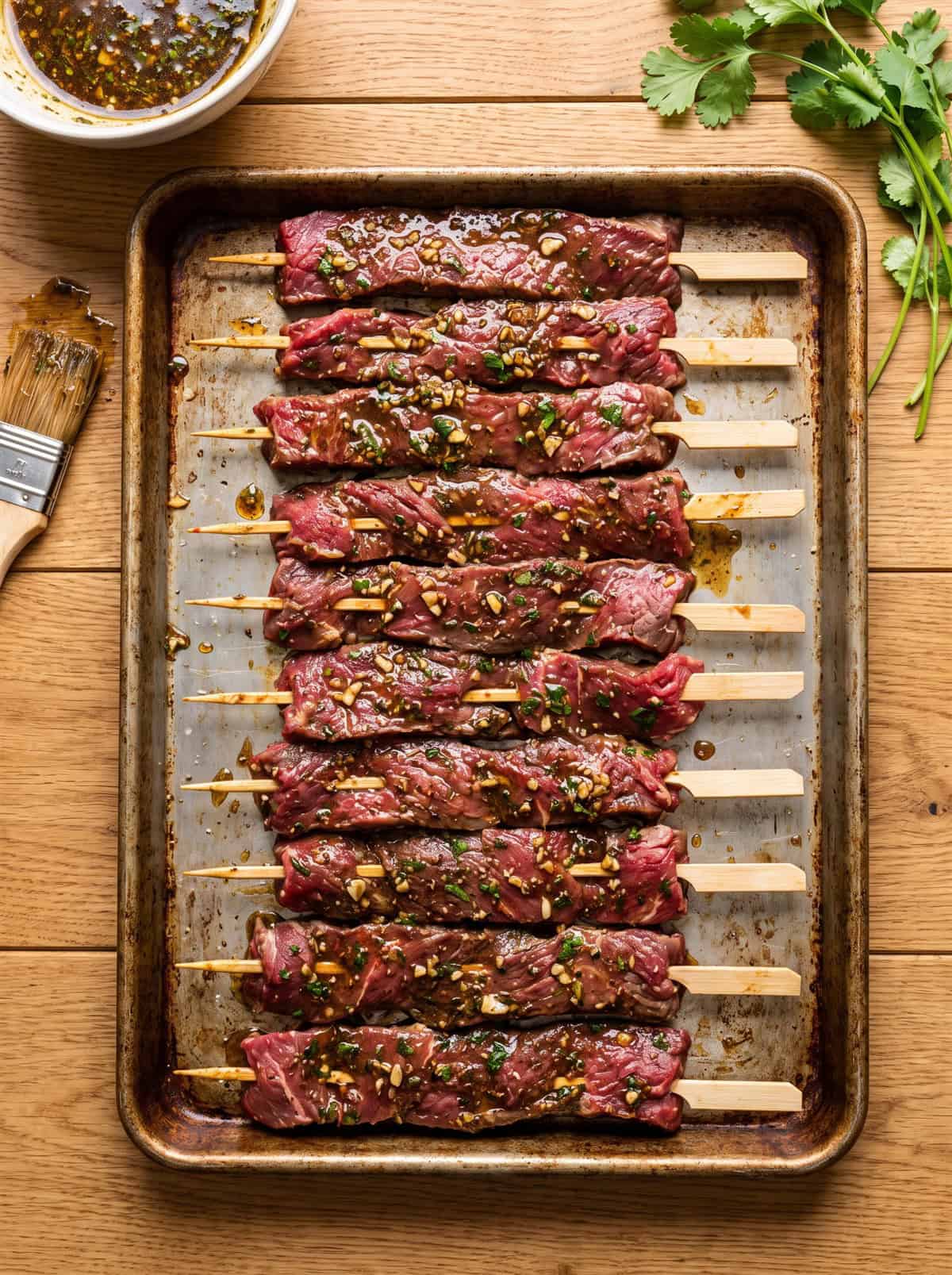 Marinated flank steak strips threaded onto wooden skewers on a tray ready to grill.