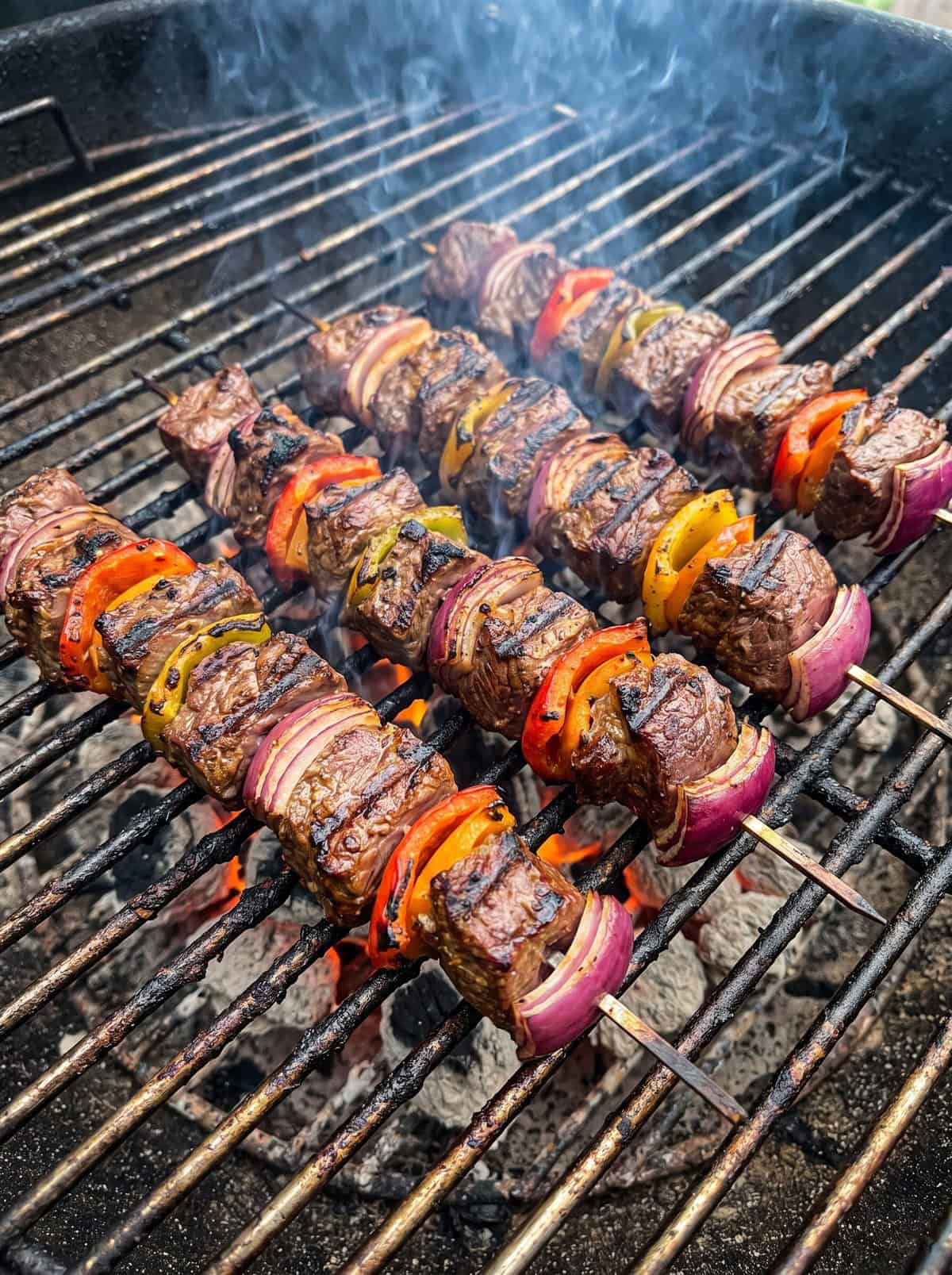 Asian beef skewers grilling on a barbecue grill with char marks.