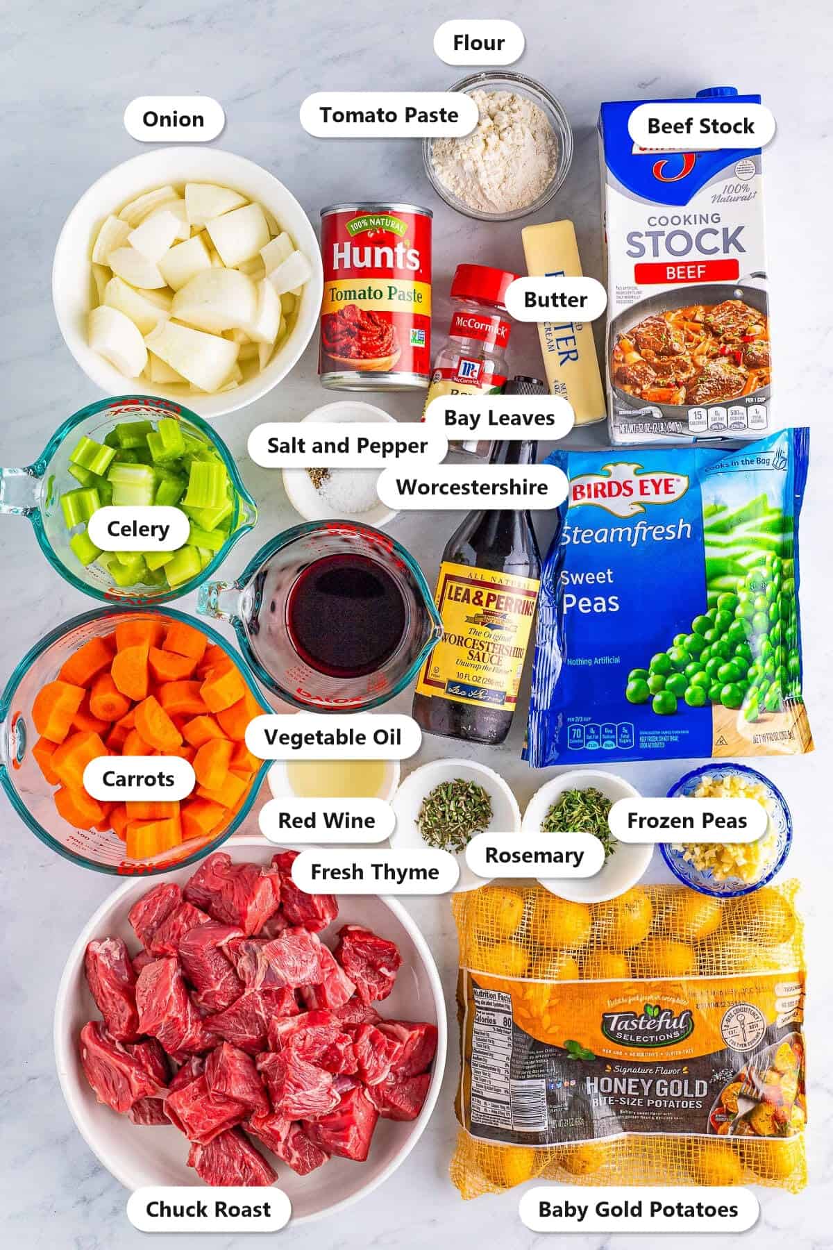 Labeled ingredients for beef stew in the oven including chuck roast, red wine, beef stock, baby gold potatoes, carrots, celery, onion, frozen peas, tomato paste, and seasonings.