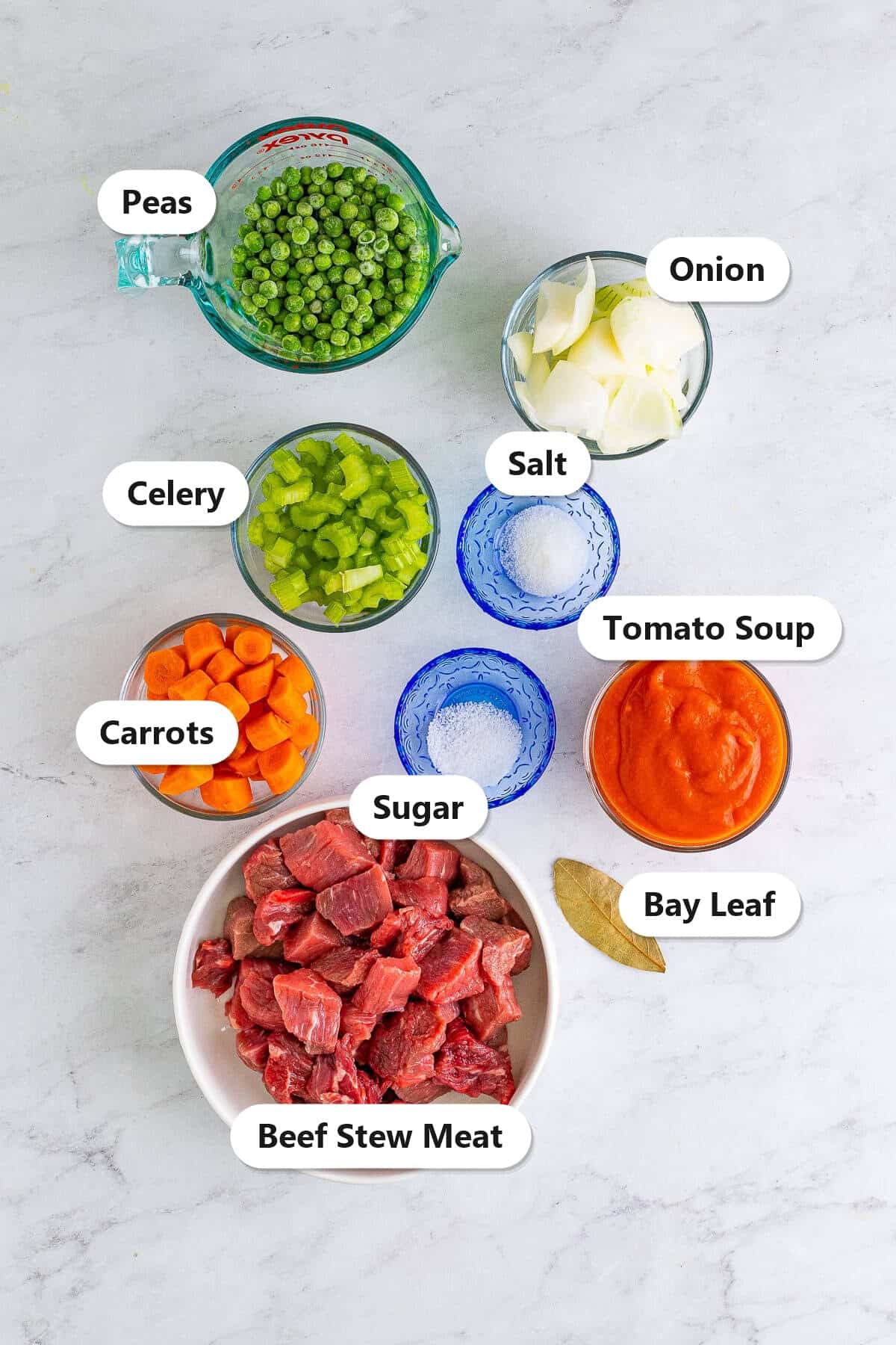 Labeled ingredients for beef stew recipe including beef stew meat, carrots, onion, celery, peas, tomato soup, salt, sugar, and a bay leaf.