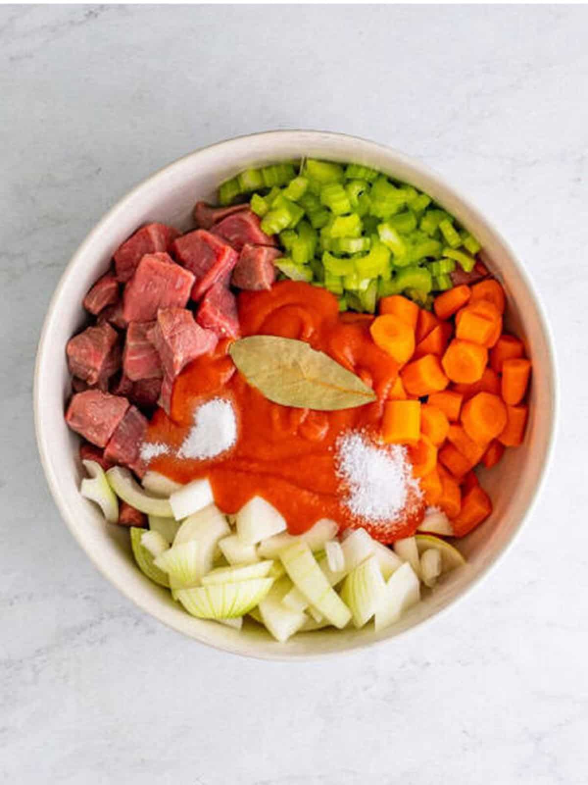 Beef stew meat, carrots, onion, celery, tomato soup, salt, and a bay leaf added to a baking dish for beef stew recipe.
