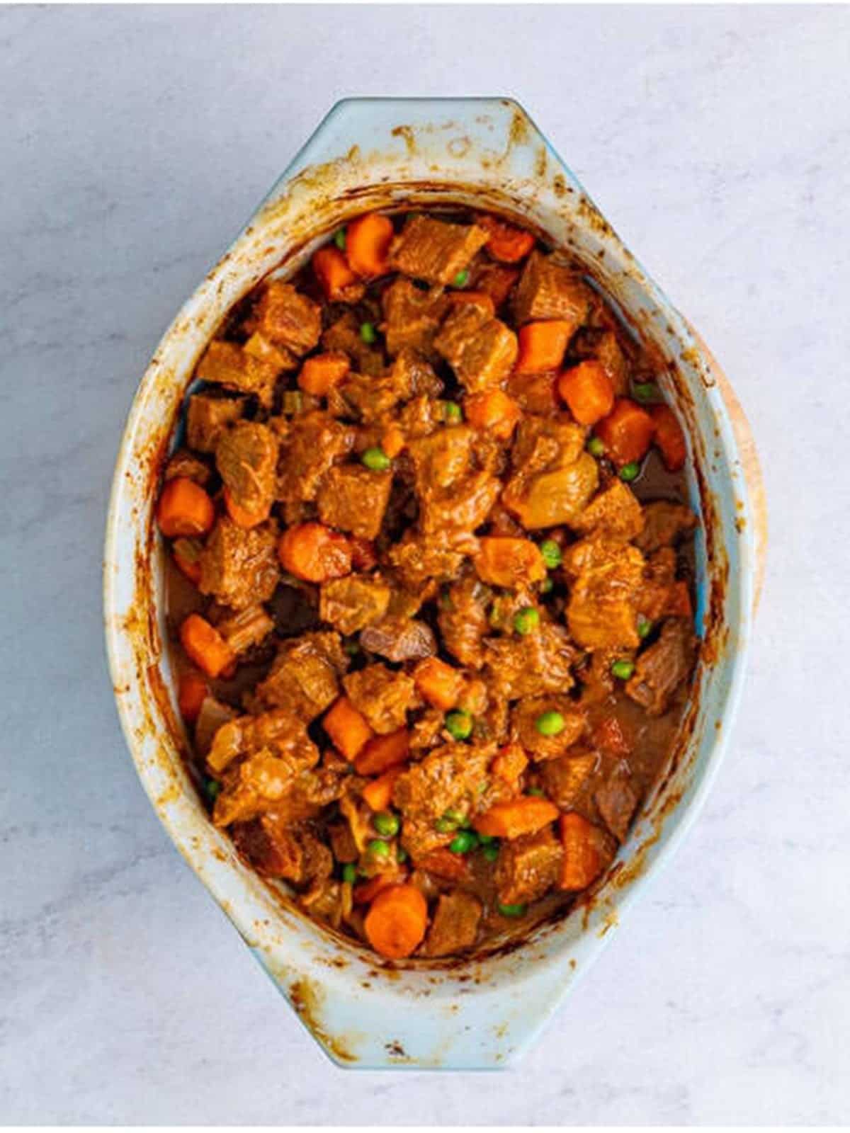 Finished oven beef stew with tender beef, carrots, and peas in a baking dish for beef stew recipe.