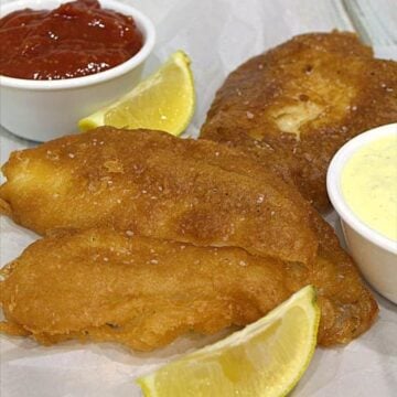 Beer batter for fish fried golden brown served with ketchup, tartar sauce, and lemon wedges.