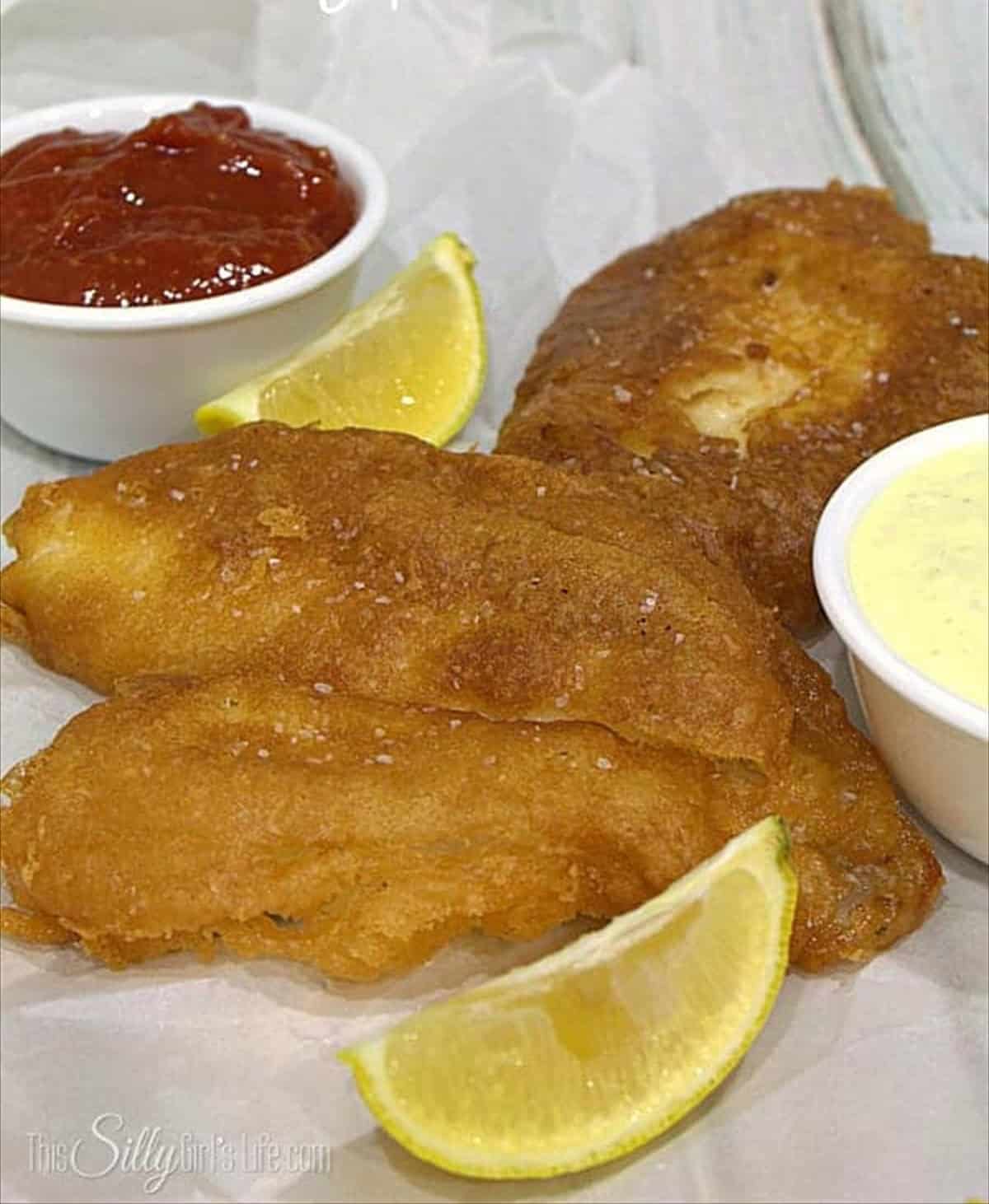 Beer batter for fish fried golden brown served with ketchup, tartar sauce, and lemon wedges.