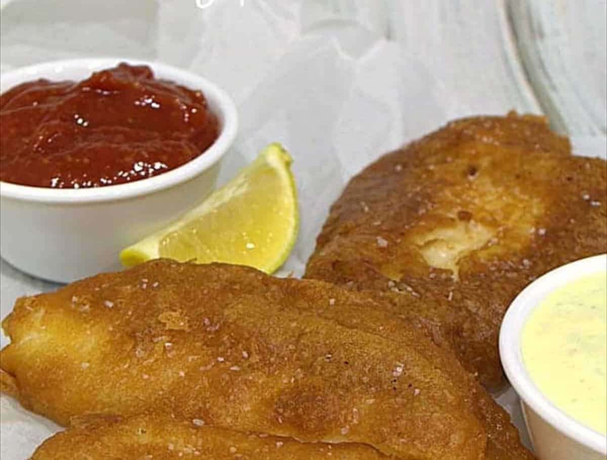 Crispy beer battered fish fillets made with Bisquick pancake mix on parchment with dipping sauce.