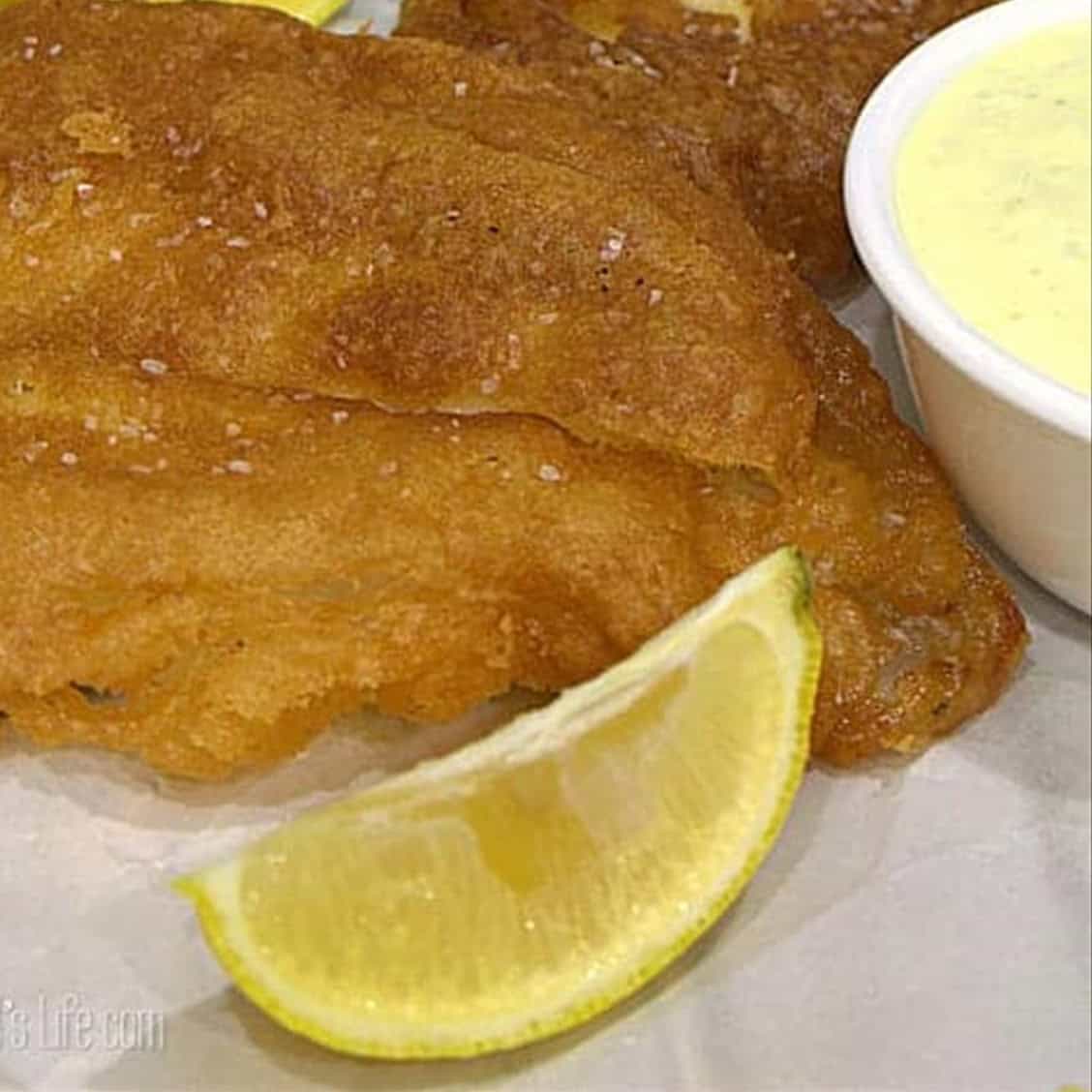 Close up of a crispy beer battered fish fillet with a lemon wedge and tartar sauce.