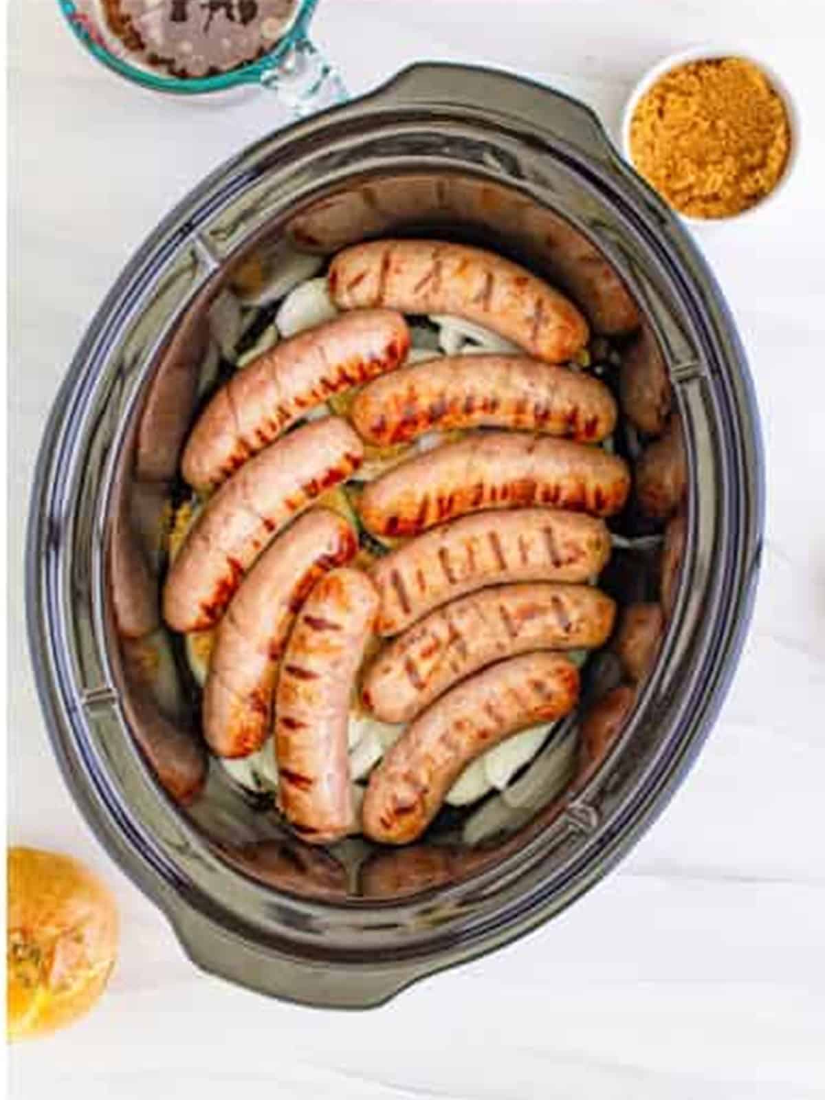 Grilled brats added to the slow cooker and topped with more onions and brown sugar.