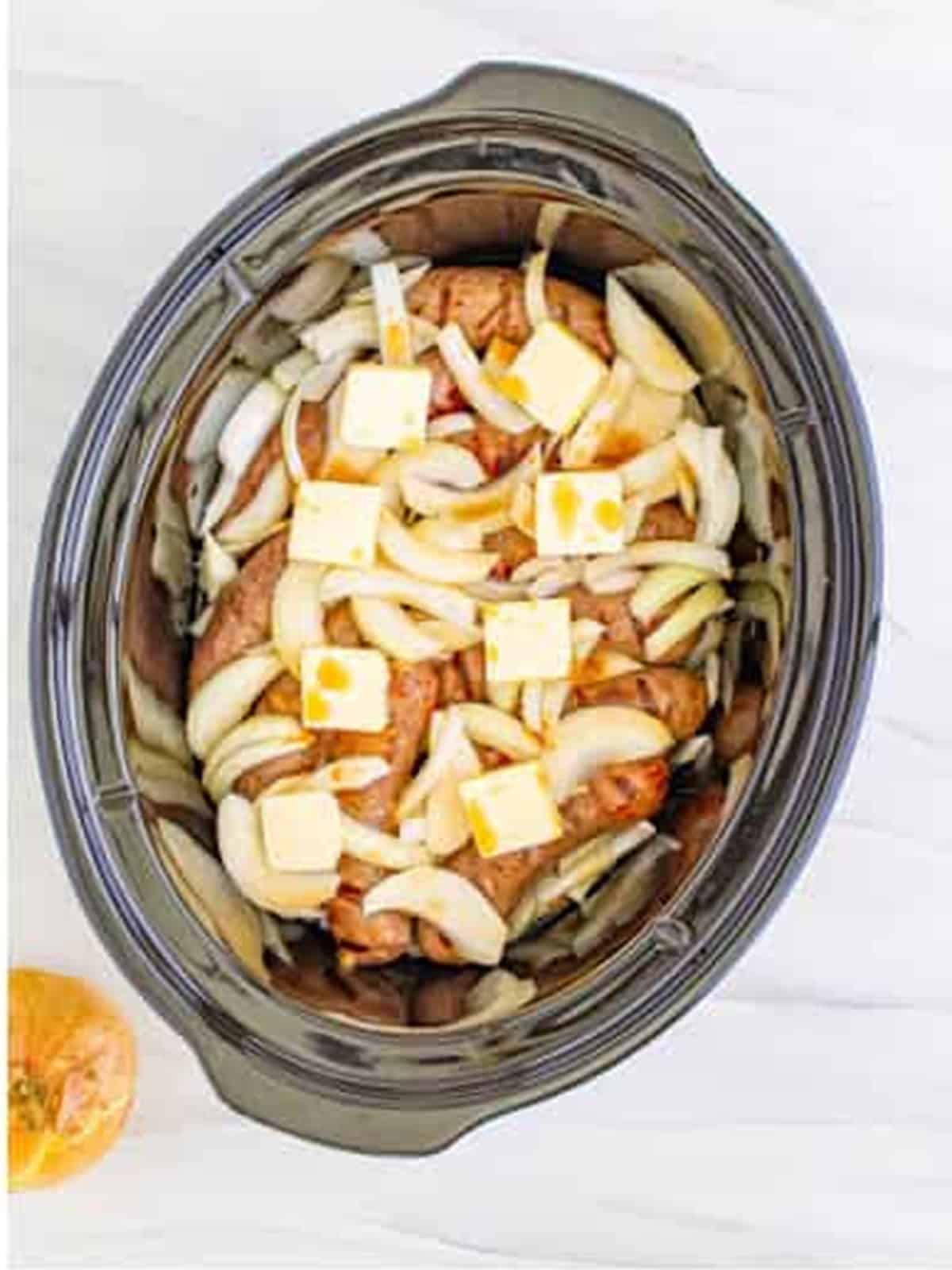 Slices of butter placed on top of brats and onions in the slow cooker.