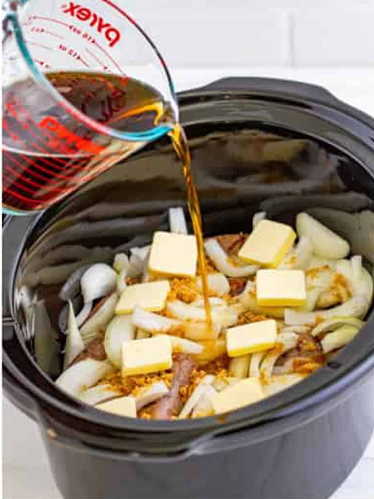 Dark beer poured over brats and onions in the slow cooker.