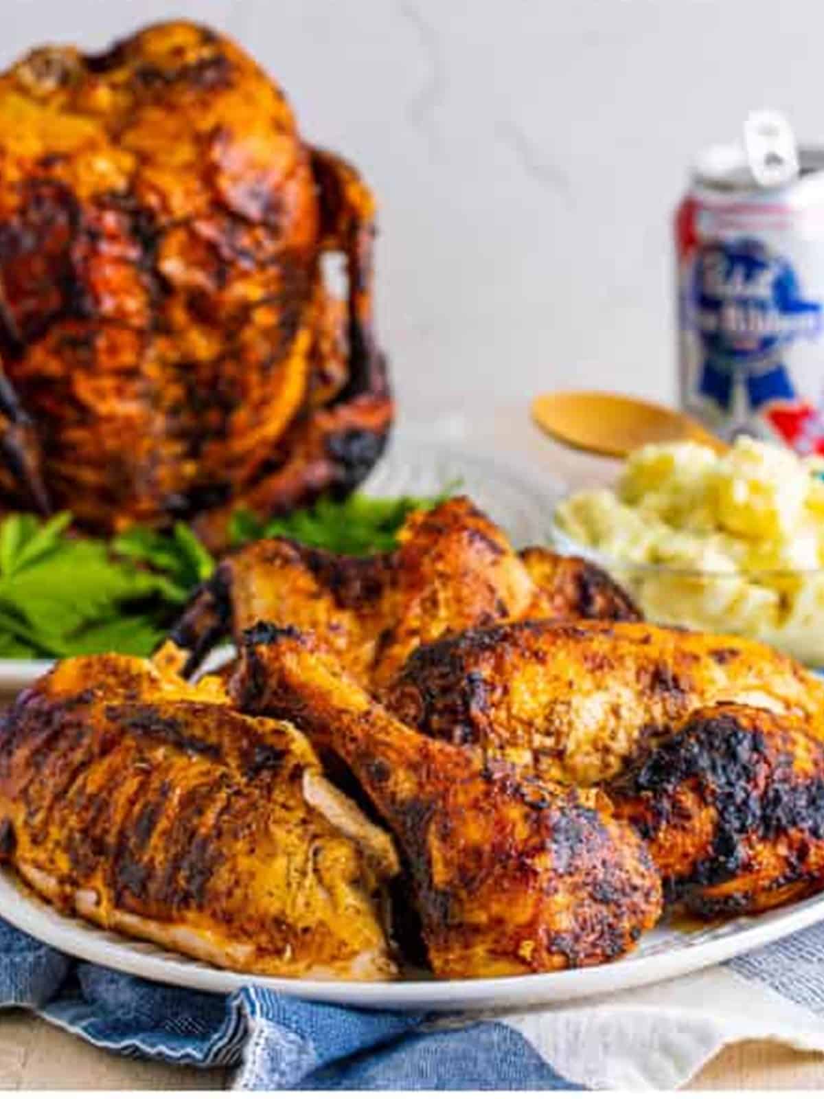 Carved beer can chicken on a white platter served with mashed potatoes.